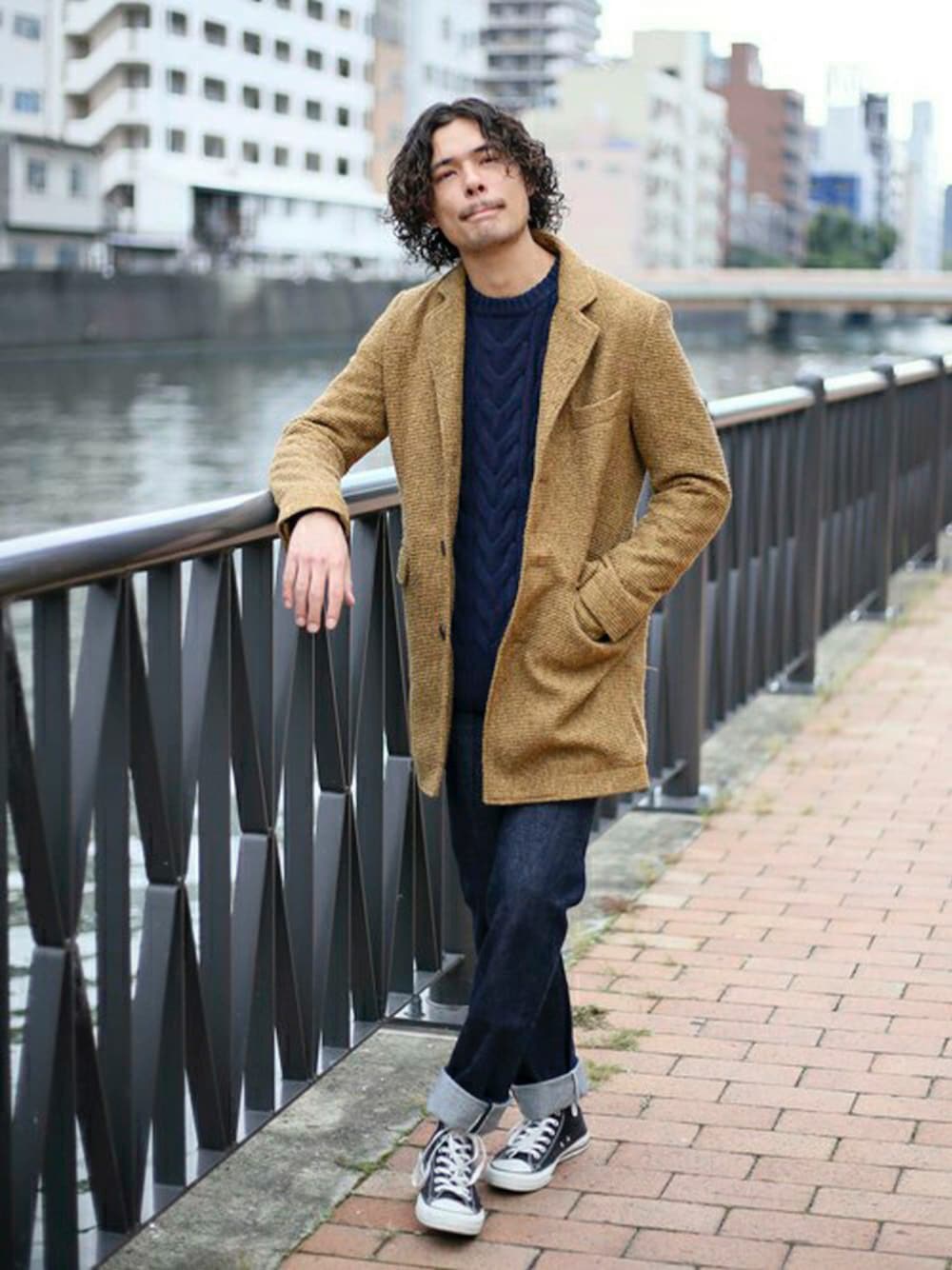 ベージュ系のチェスターコート、ブルー系のニット/セーター、ブルー系のデニムパンツを着用したメンズの冬コーディネートの1枚目の写真