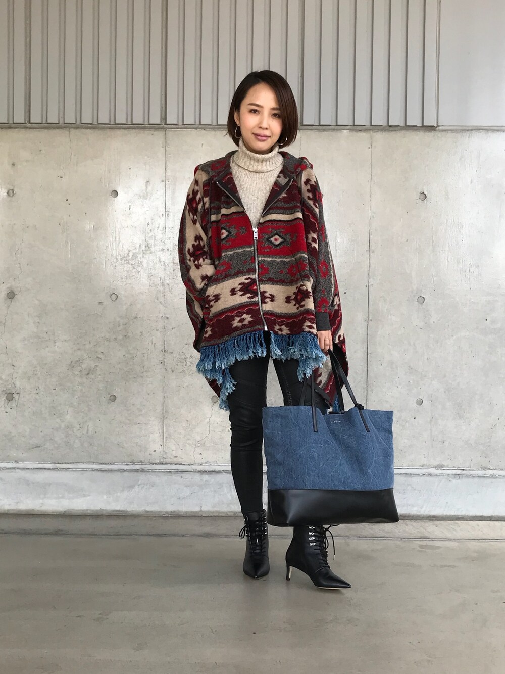 レッド系のポンチョ、ホワイト系のニット/セーター、ブラック系のデニムパンツを着用したレディースの秋コーディネートの1枚目の写真