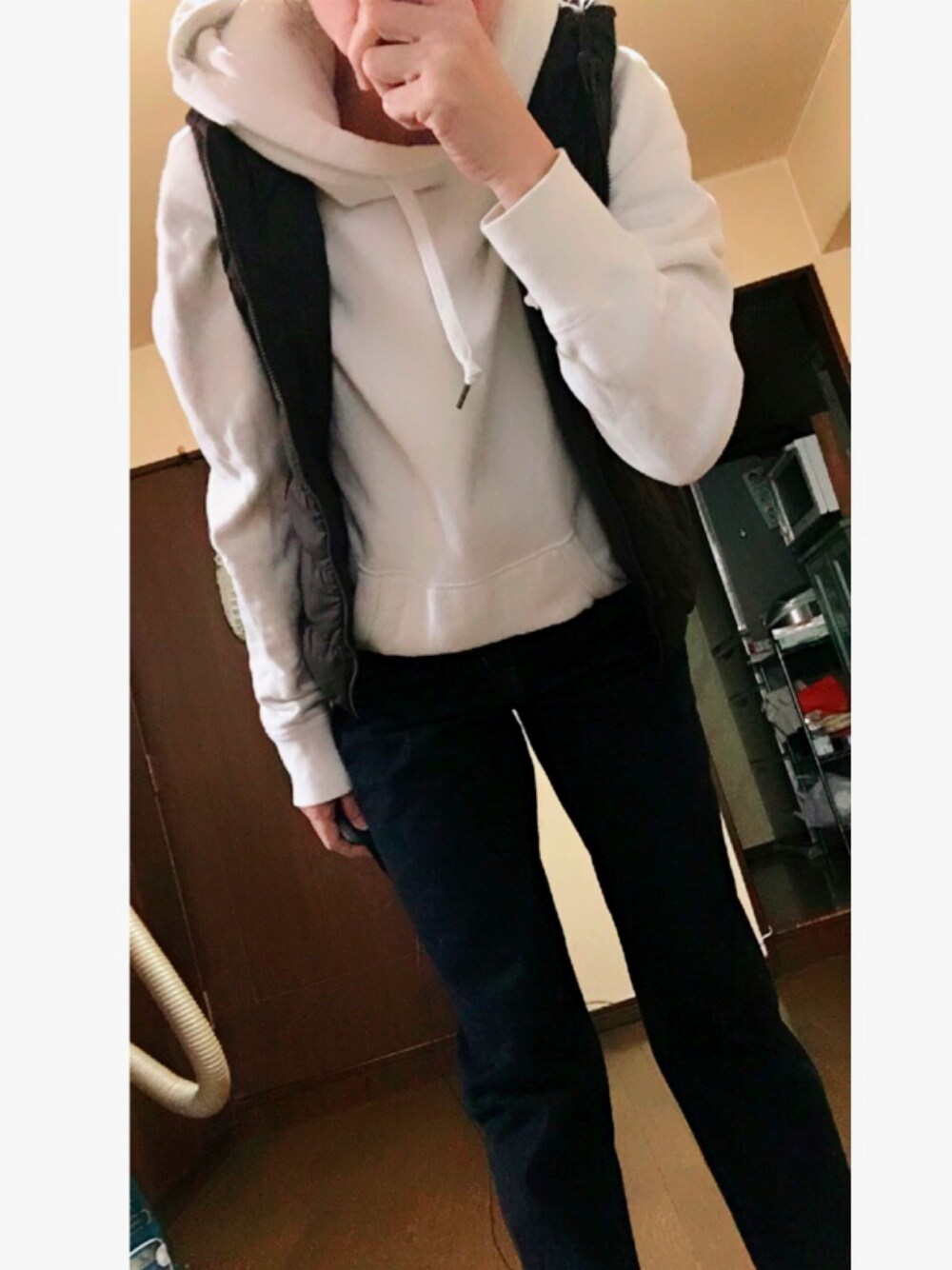 ホワイト系のパーカー、ブラウン系のダウンベスト、ブルー系のデニムパンツを着用したレディースの秋コーディネートの1枚目の写真