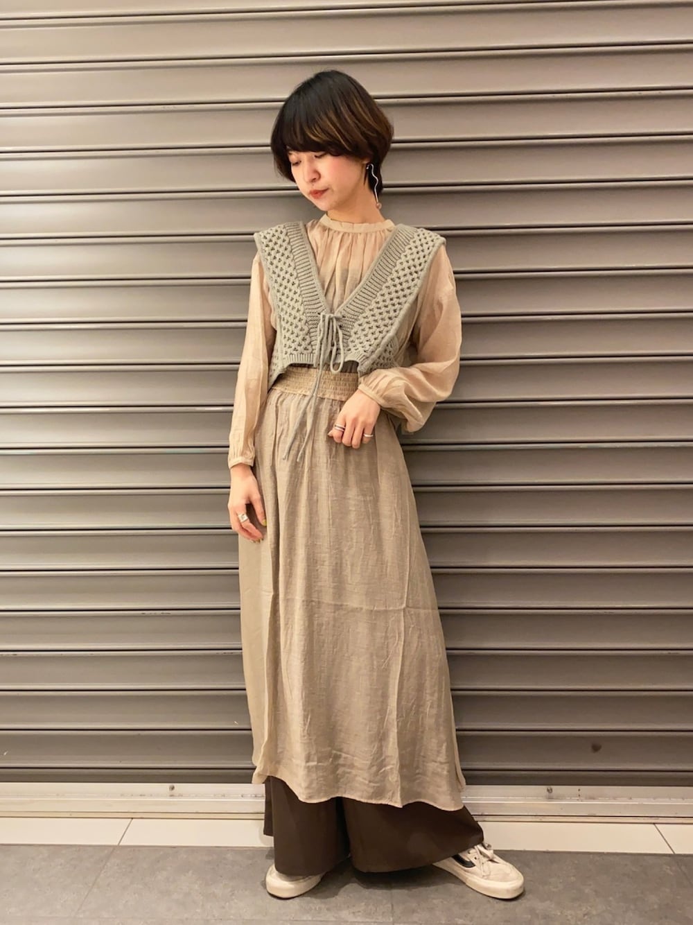 グリーン系のベスト、ベージュ系のワンピース、ホワイト系のスニーカーを着用したレディースの春コーディネートの1枚目の写真