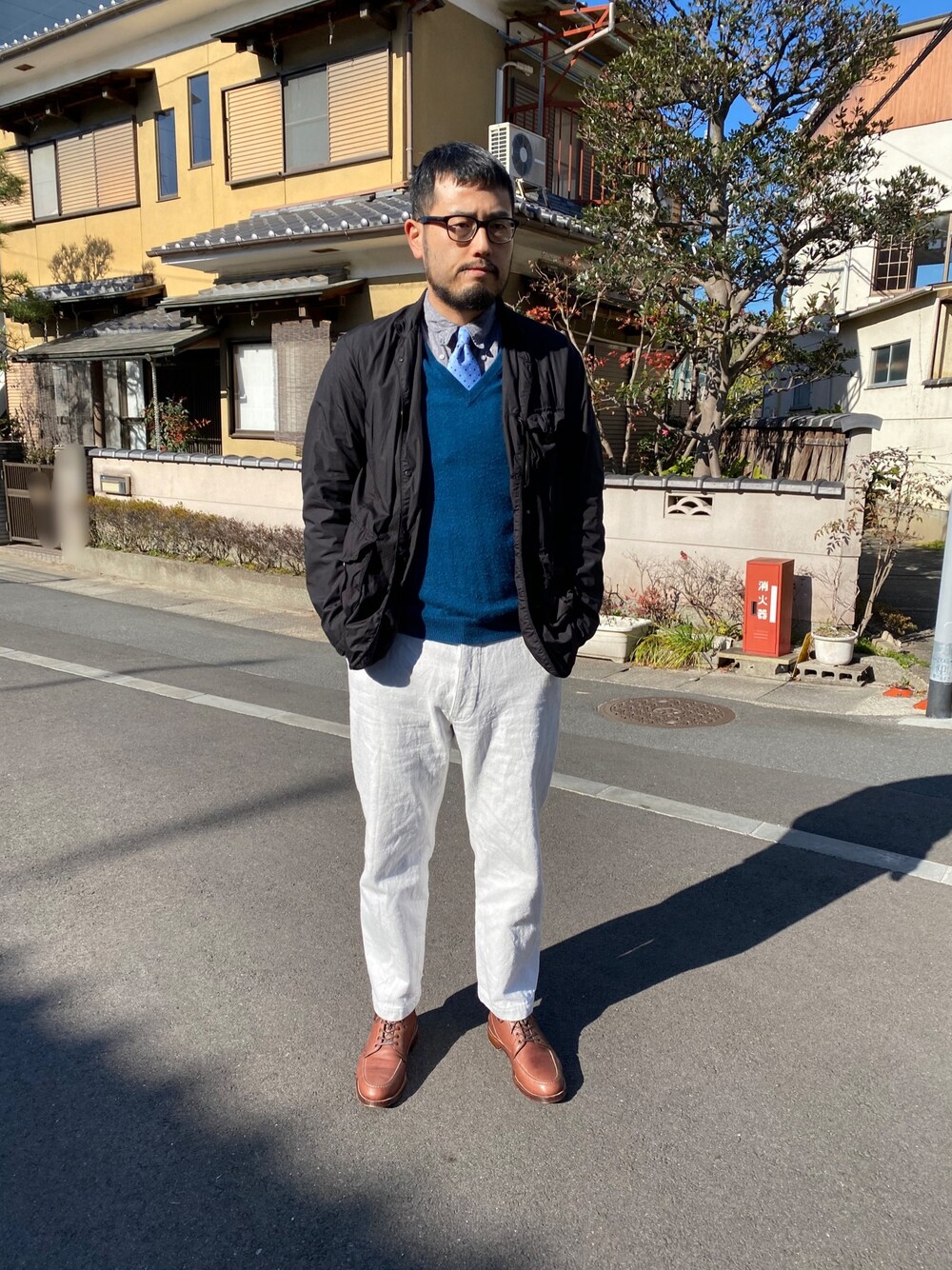 ブラック系のテーラードジャケット、ブルー系のニット/セーター、ホワイト系のデニムパンツを着用したメンズの春コーディネートの1枚目の写真