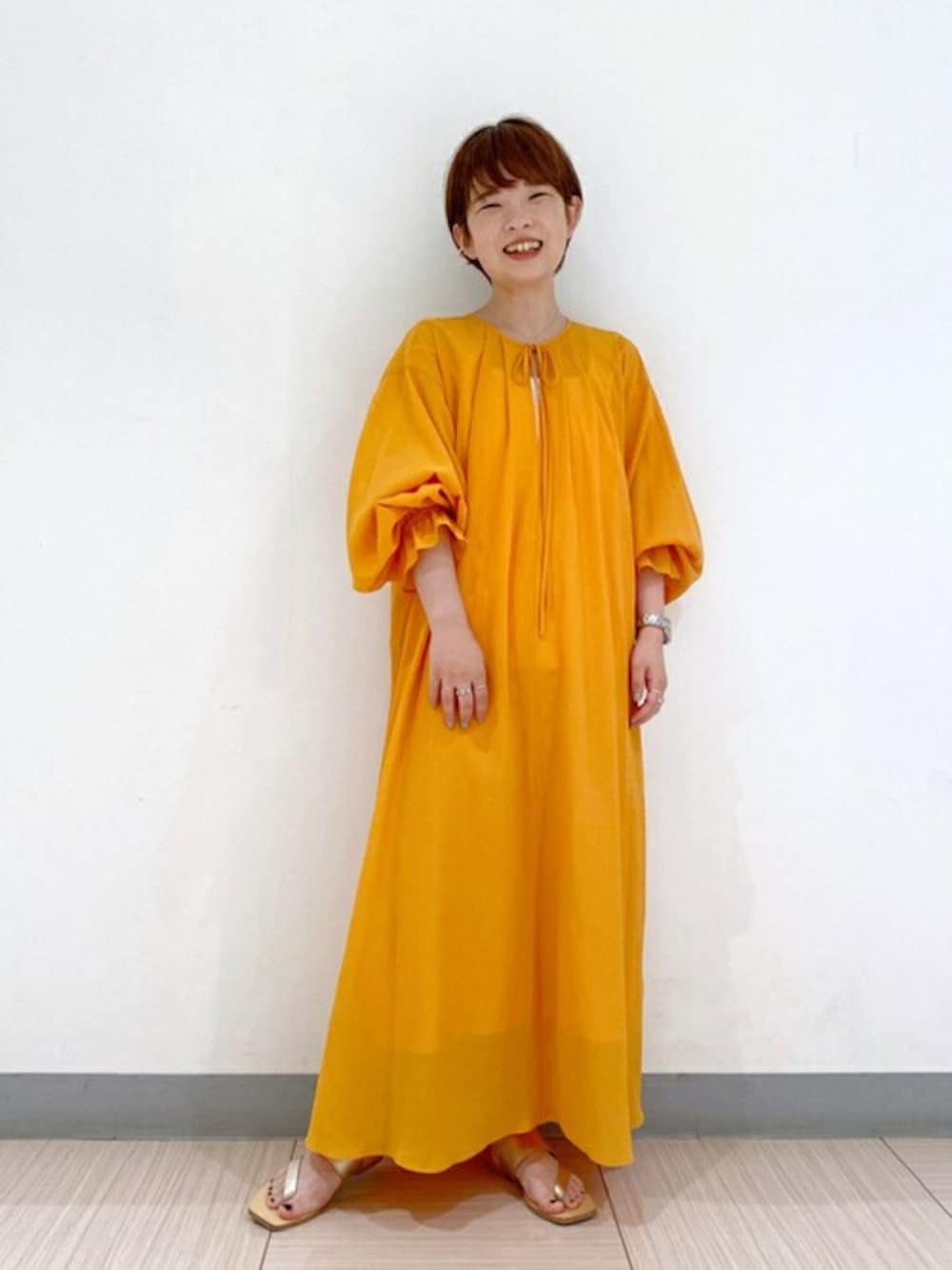 オレンジ系のワンピース、ゴールド系のサンダル、ゴールド系のイヤーカフを着用したレディースの夏コーディネートの1枚目の写真