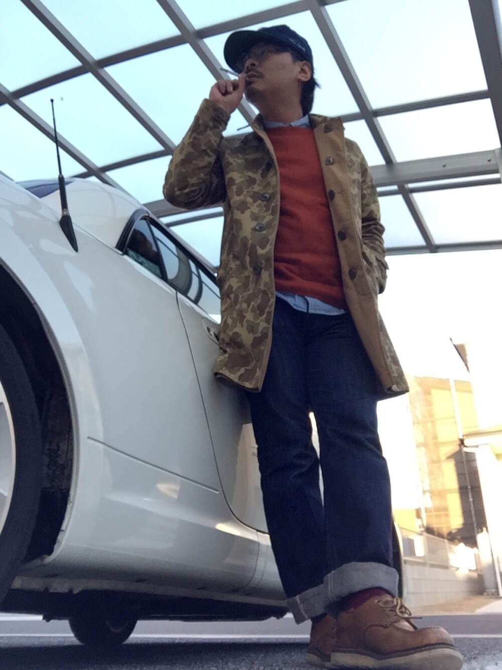 ベージュ系のステンカラーコート、レッド系のニット/セーター、ブルー系のシャツ/ブラウスを着用したメンズの冬コーディネートの1枚目の写真