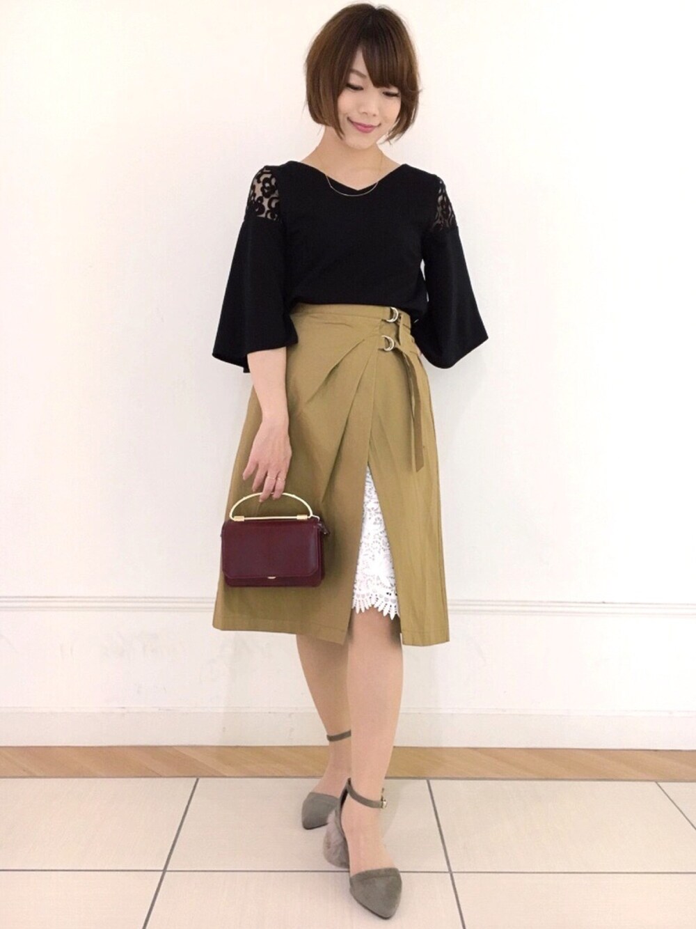 ベージュ系のスカート、グリーン系のパンプス、レッド系のショルダーバッグを着用したレディースの夏コーディネートの1枚目の写真