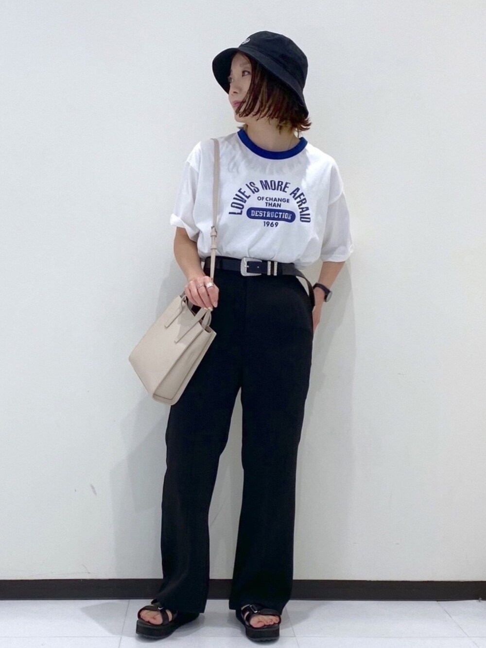 ホワイト系のTシャツ/カットソー、ブラック系のスラックス、ベージュ系のショルダーバッグを着用したレディースの春コーディネートの1枚目の写真