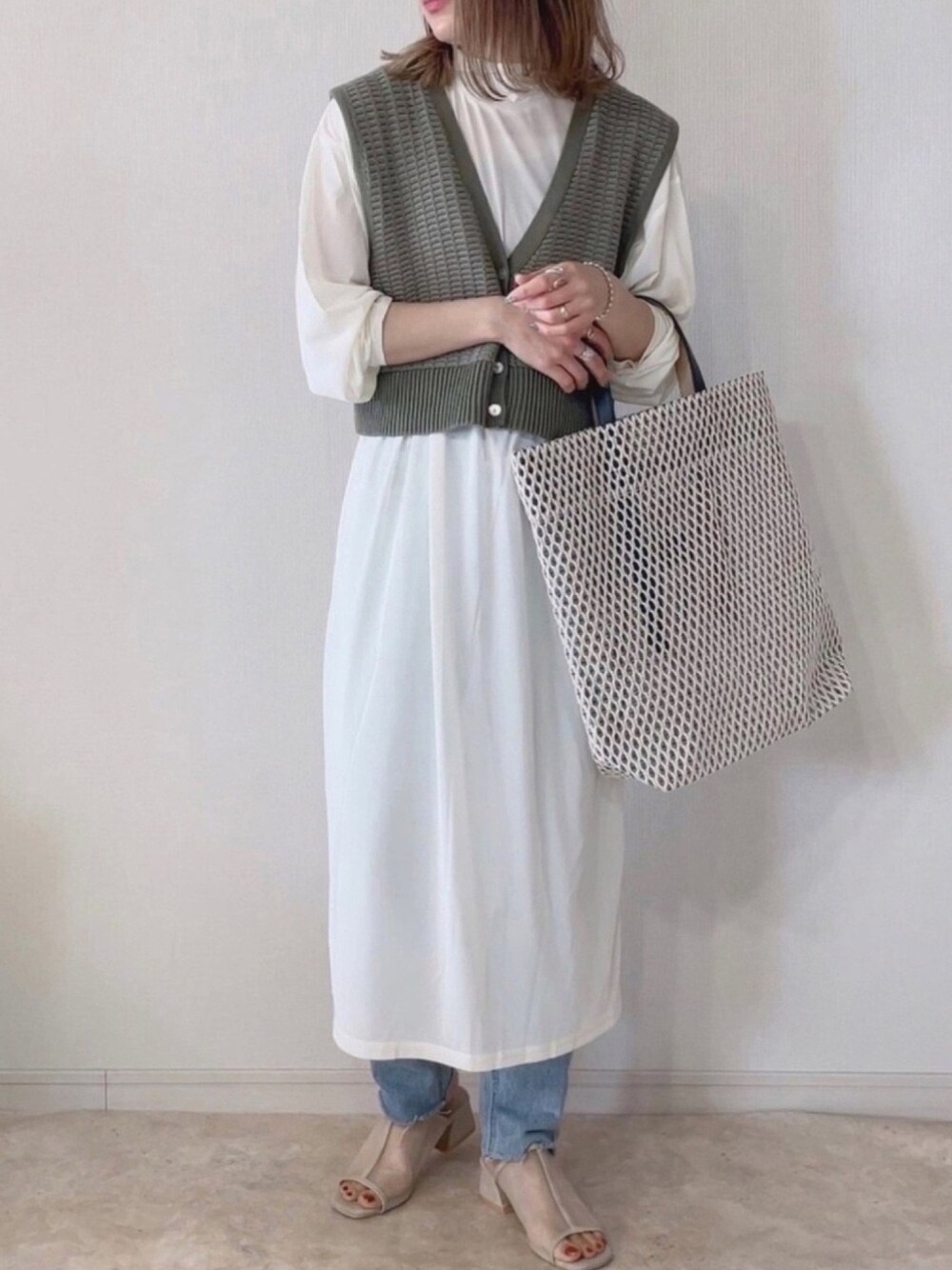 ホワイト系のワンピース、グリーン系のベスト、ベージュ系のサンダルを着用したレディースの春コーディネートの1枚目の写真