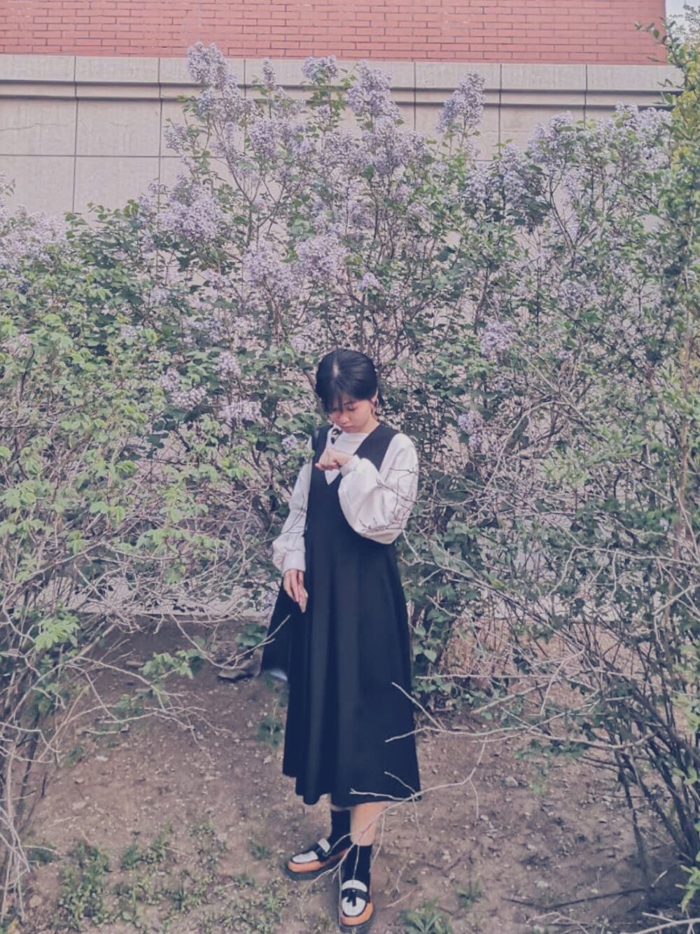 ホワイト系のTシャツ/カットソー、ブラック系のジャンパースカート、ブラック系のクラッチバッグを着用したレディースの春コーディネートの1枚目の写真