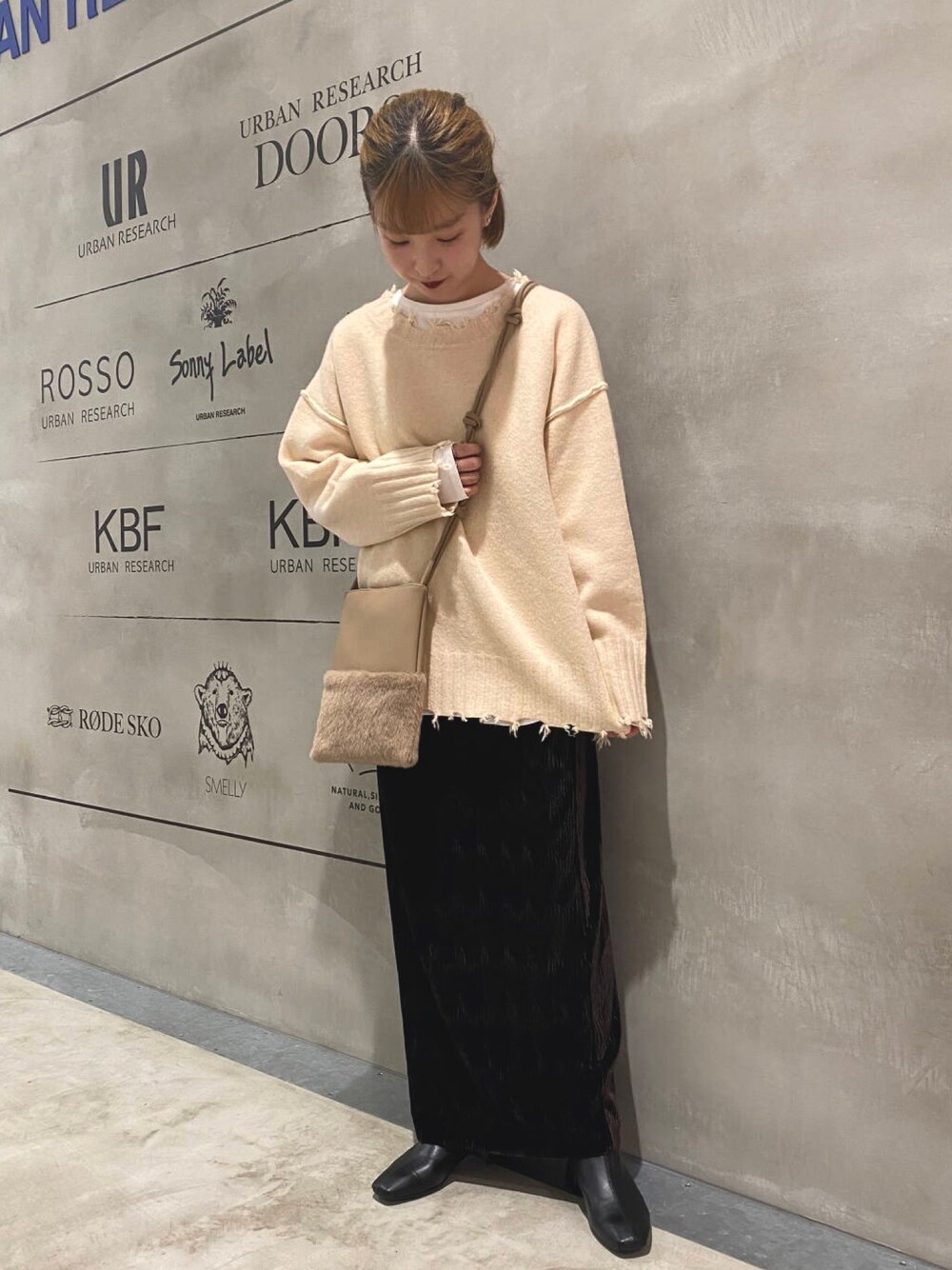 ホワイト系のニット/セーター、ブラウン系のスカート、ベージュ系のショルダーバッグを着用したレディースの冬コーディネートの1枚目の写真