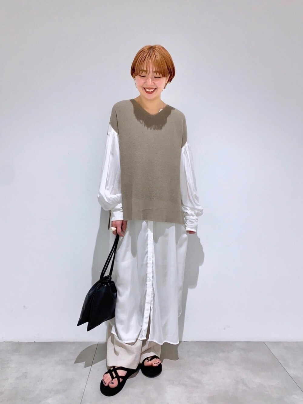 グレー系のベスト、ホワイト系のワンピース、ベージュ系のその他パンツを着用したレディースの春コーディネートの1枚目の写真