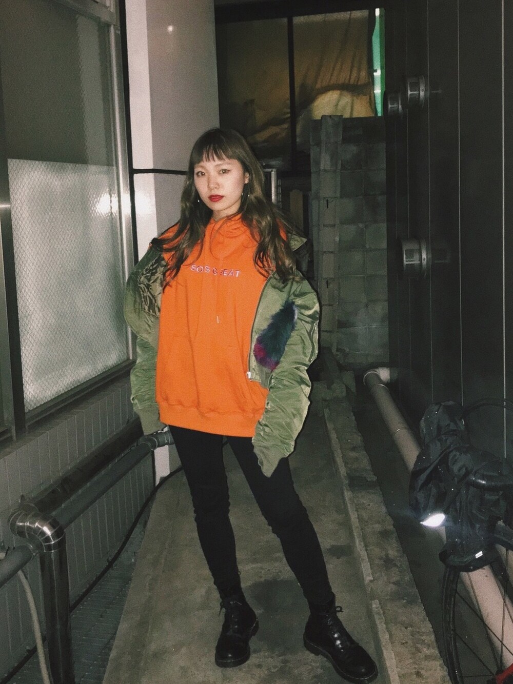 オレンジ系のパーカー、グリーン系のミリタリージャケット、ブラック系のブーツを着用したレディースの冬コーディネートの1枚目の写真