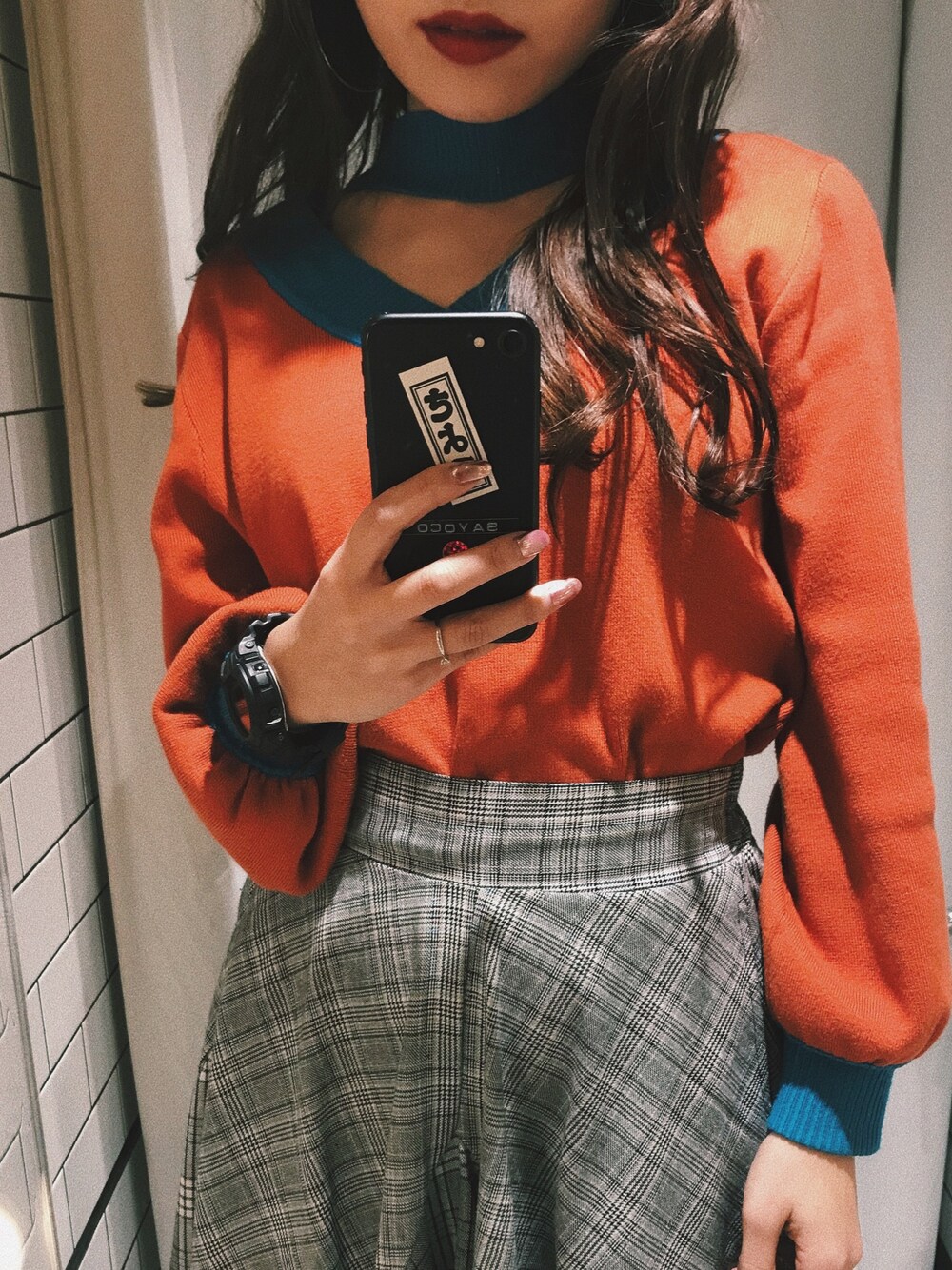 オレンジ系のニット/セーター、グレー系のスカート、ブラック系のデジタル腕時計を着用したレディースの冬コーディネートの1枚目の写真