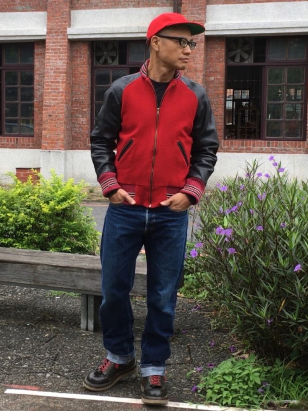 レッド系のスタジャン、ブラック系のブーツ、ブルー系のデニムパンツを着用したメンズの秋コーディネートの1枚目の写真