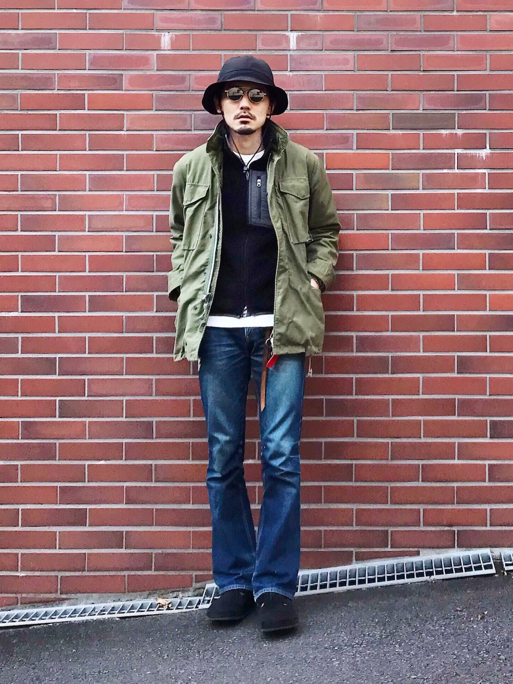 グリーン系のミリタリージャケット、ブラック系のベスト、ブルー系のデニムパンツを着用したメンズの秋コーディネートの1枚目の写真