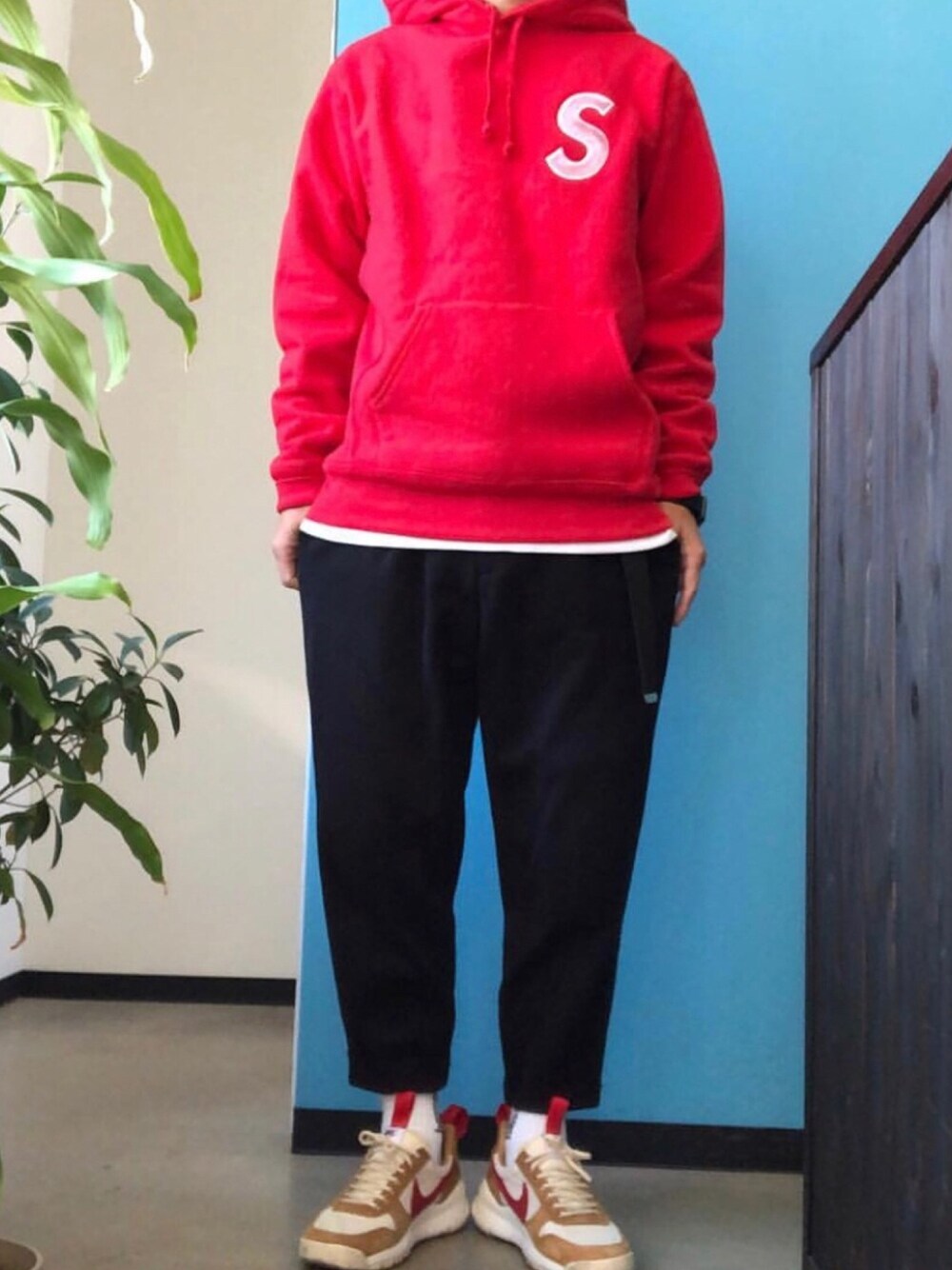 レッド系のパーカー、ブラック系のパンツ、ベージュ系のスニーカーを着用したメンズの冬コーディネートの1枚目の写真