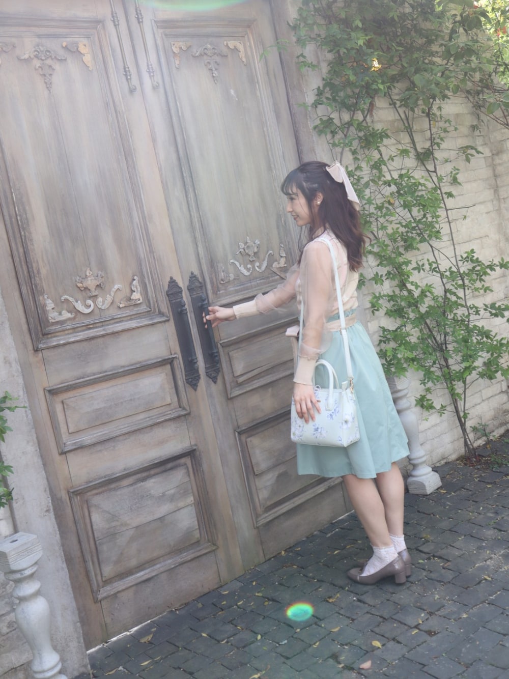 ベージュ系のニット/セーター、グリーン系のスカート、ブルー系のショルダーバッグを着用したレディースの春コーディネートの1枚目の写真