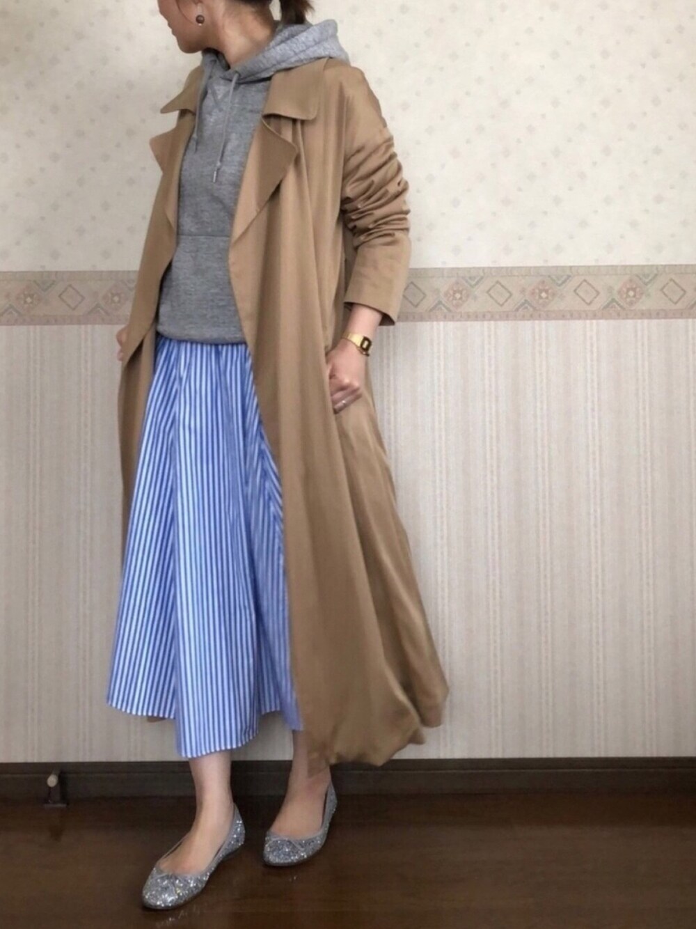 ブルー系のスカート、ベージュ系のトレンチコート、グレー系のピアス（両耳用）を着用したレディースの春コーディネートの1枚目の写真