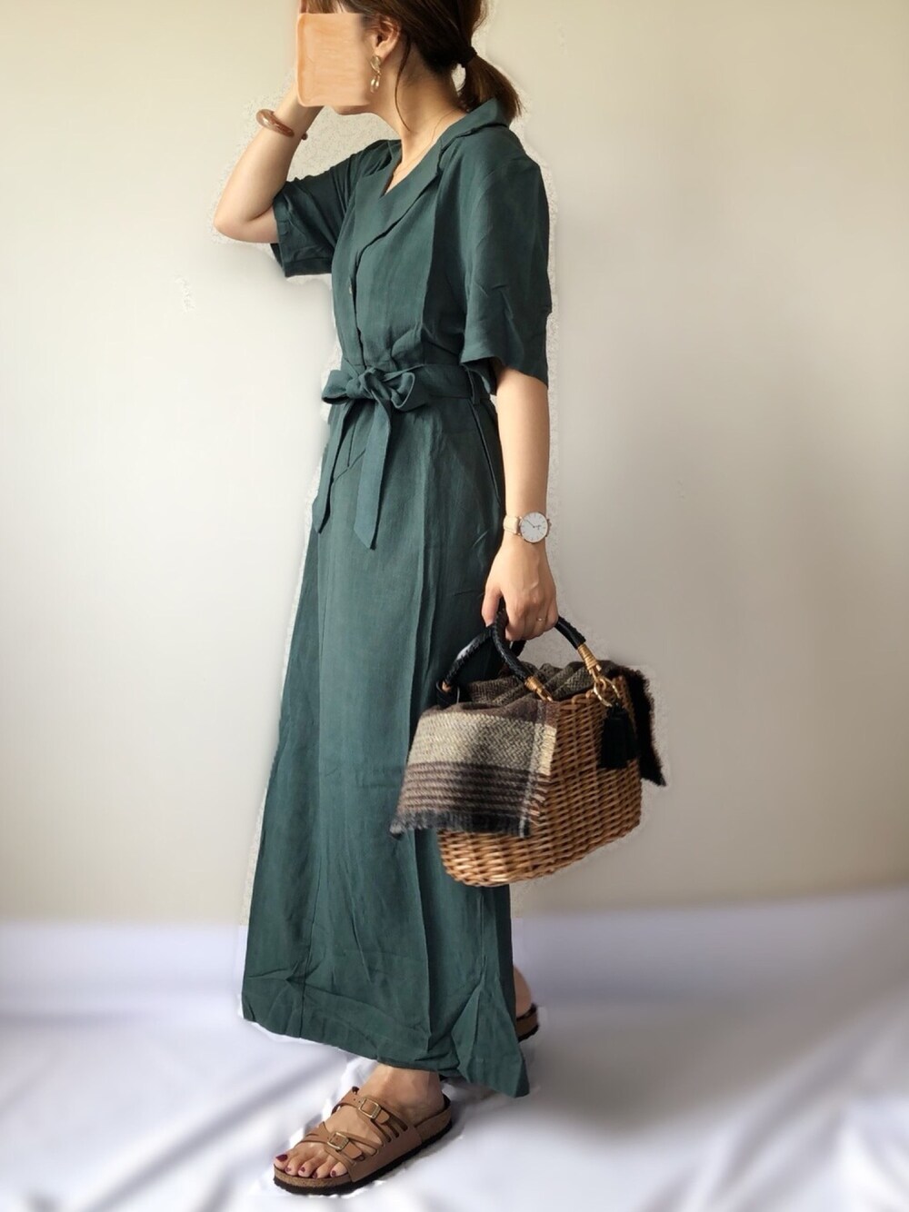 グリーン系のワンピース、ブラック系のかごバッグ、ブラウン系のサンダルを着用したレディースの秋コーディネートの1枚目の写真