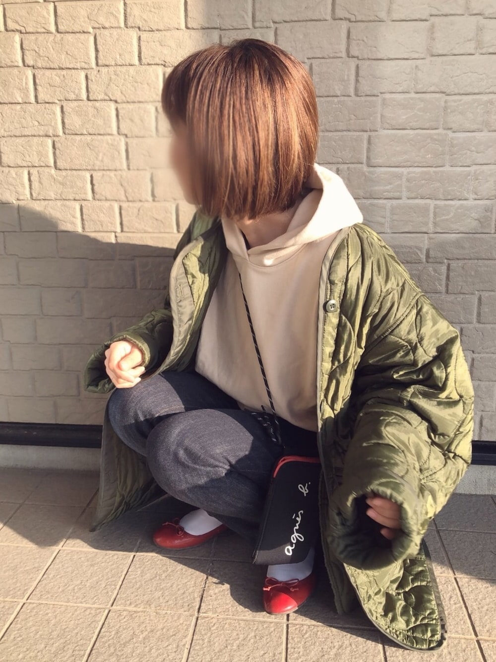 グリーン系のミリタリージャケット、ベージュ系のパーカー、ブルー系のデニムパンツを着用したレディースの冬コーディネートの1枚目の写真