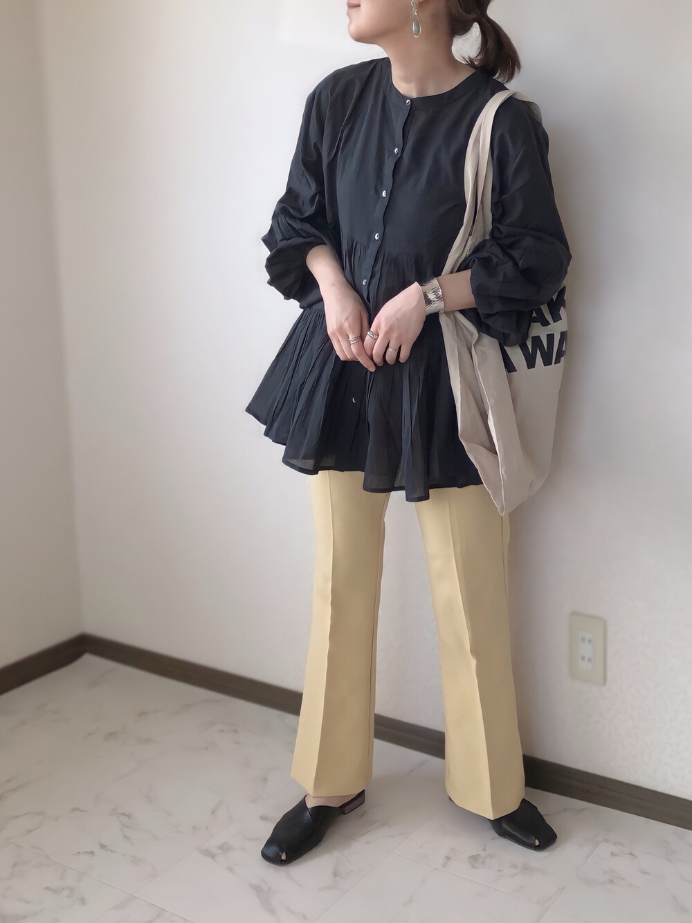 ブラック系のシャツ/ブラウス、イエロー系のスラックス、ベージュ系のトートバッグを着用したレディースの春コーディネートの1枚目の写真