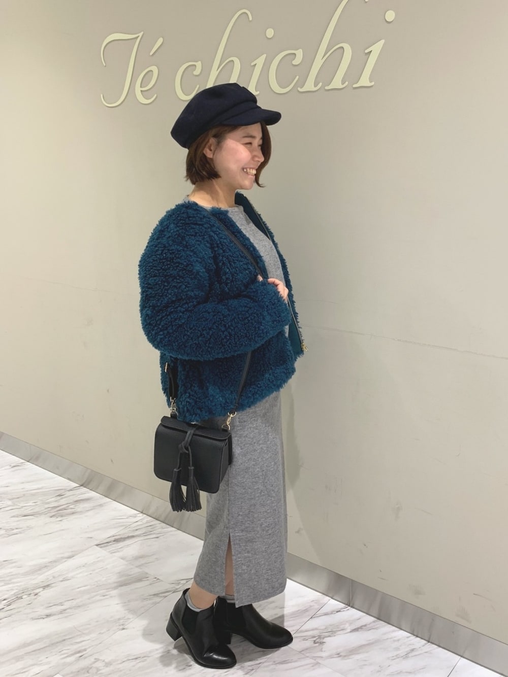 グレー系のスカート、ブラック系のブーティ、ブラック系のショルダーバッグを着用したレディースの秋コーディネートの1枚目の写真