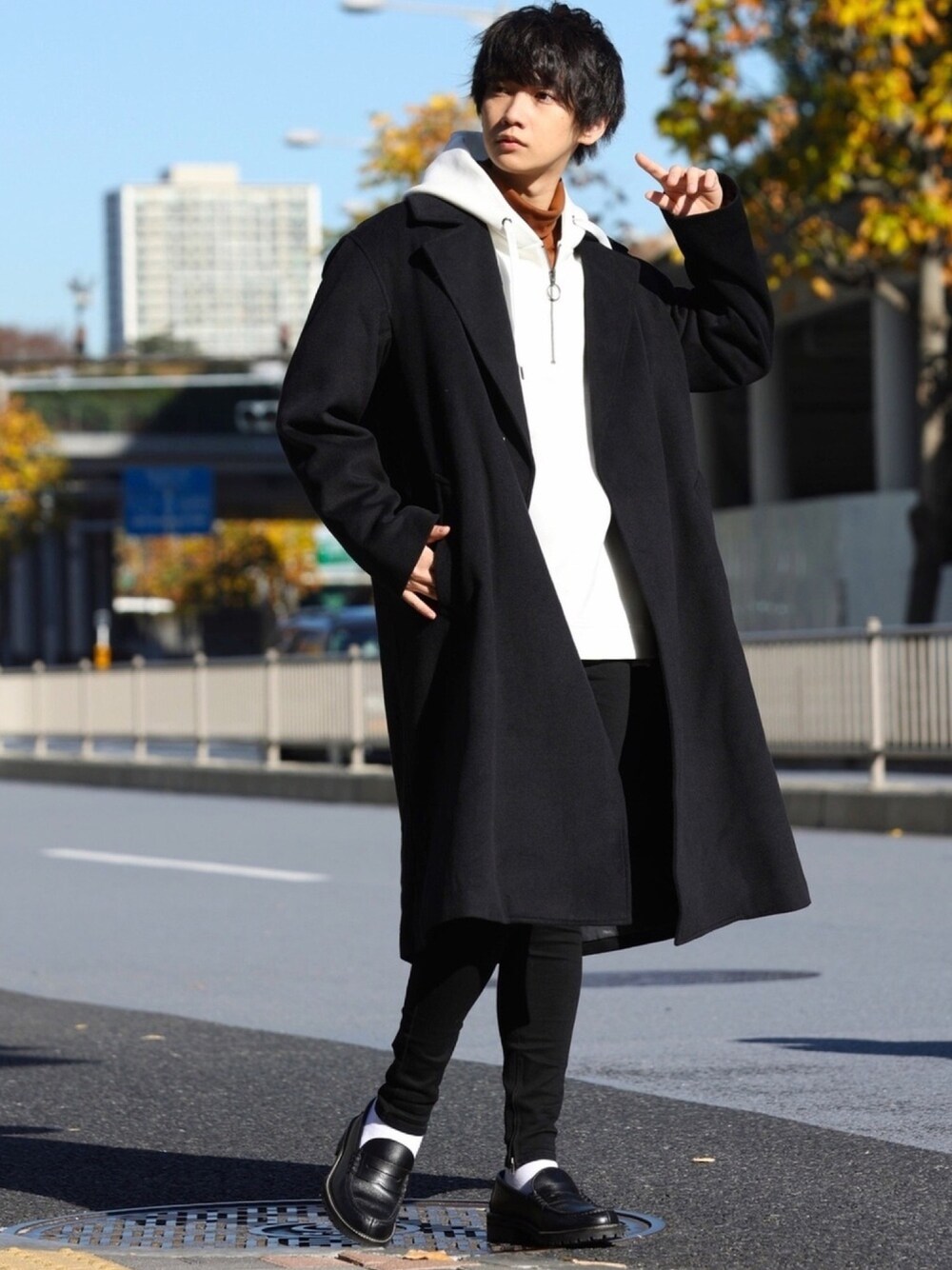 ブラック系のチェスターコート、ベージュ系のパーカー、ブラウン系のTシャツ/カットソーを着用したメンズの冬コーディネートの1枚目の写真