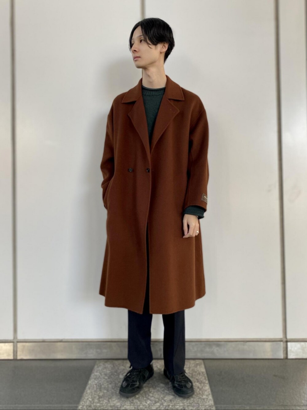 ブラウン系のその他アウター、グリーン系のニット/セーター、ブラック系のスラックスを着用したメンズの秋コーディネートの1枚目の写真