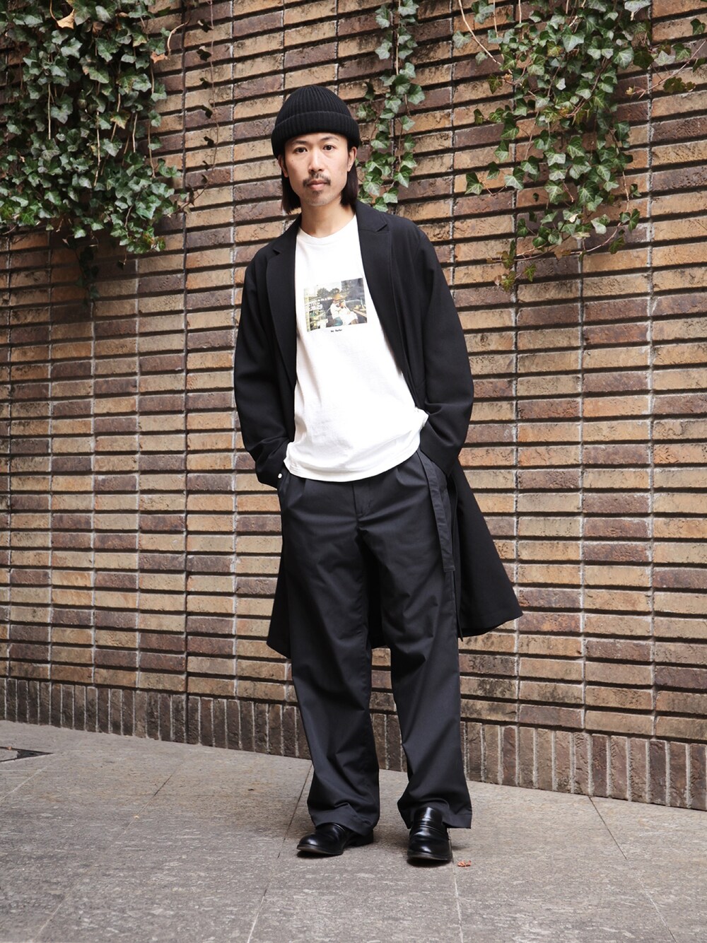 ブラック系のチェスターコート、ホワイト系のTシャツ/カットソー、ブラック系のその他パンツを着用したメンズの春コーディネートの1枚目の写真