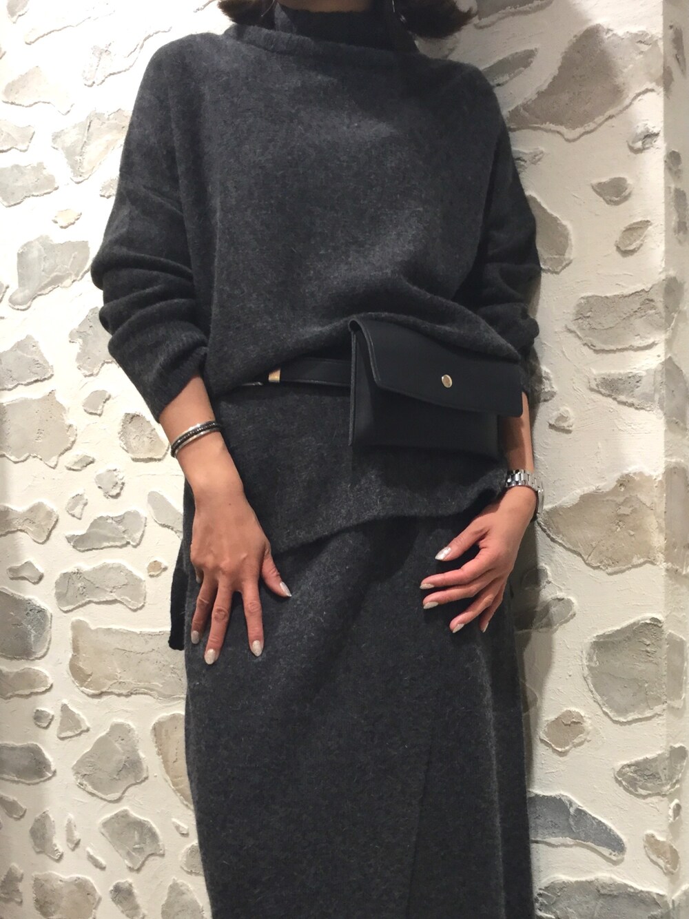 グレー系のニット/セーター、グレー系のスカート、ブラック系のバングル/リストバンドを着用したレディースの秋コーディネートの1枚目の写真