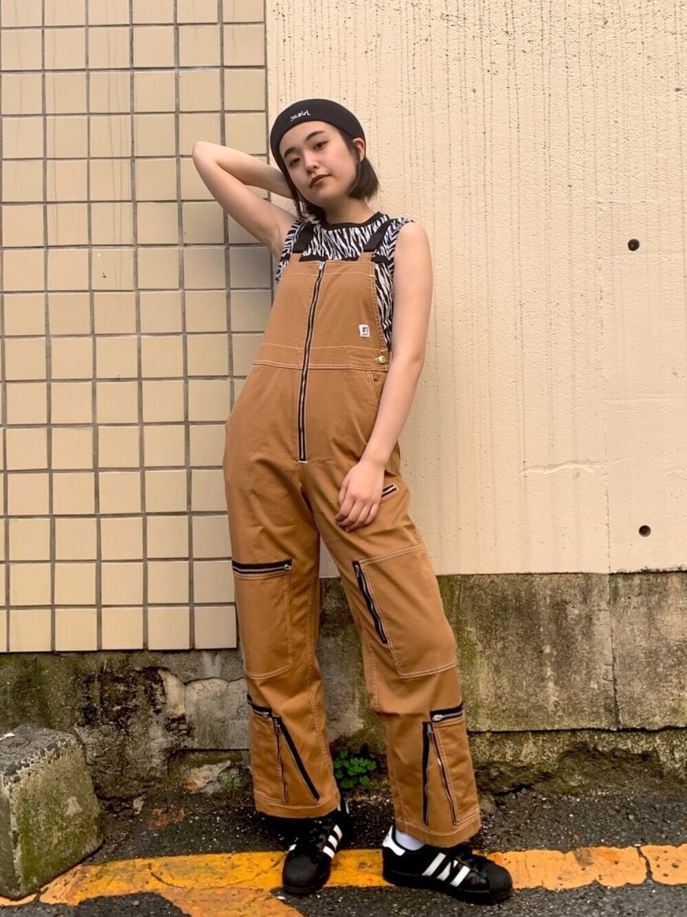 ベージュ系のサロペット/オーバーオール、ホワイト系のタンクトップ、ブラック系のスニーカーを着用したレディースの春コーディネートの1枚目の写真