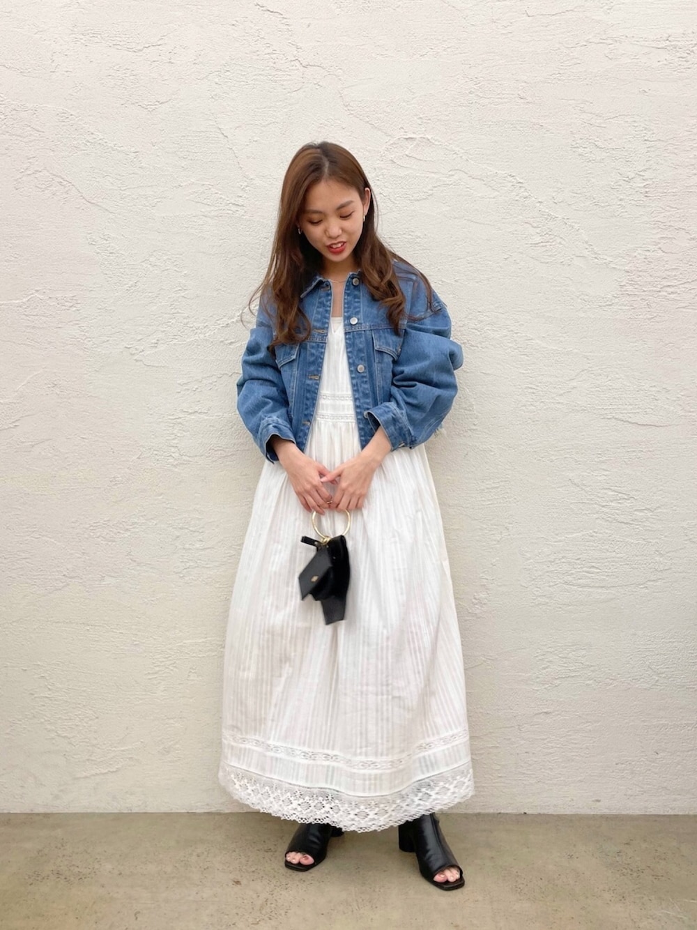 ブルー系のデニムジャケット、ホワイト系のワンピース、ブラック系のショルダーバッグを着用したレディースの春コーディネートの1枚目の写真