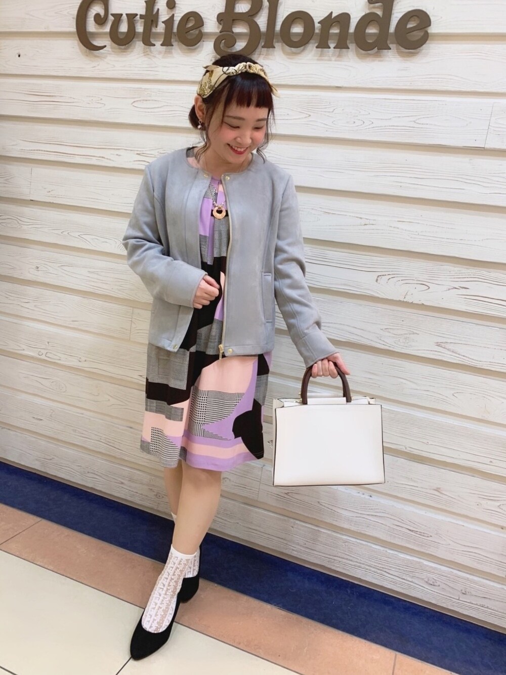 グレー系のノーカラージャケット、パープル系のワンピース、ホワイト系のショルダーバッグを着用したレディースの春コーディネートの1枚目の写真