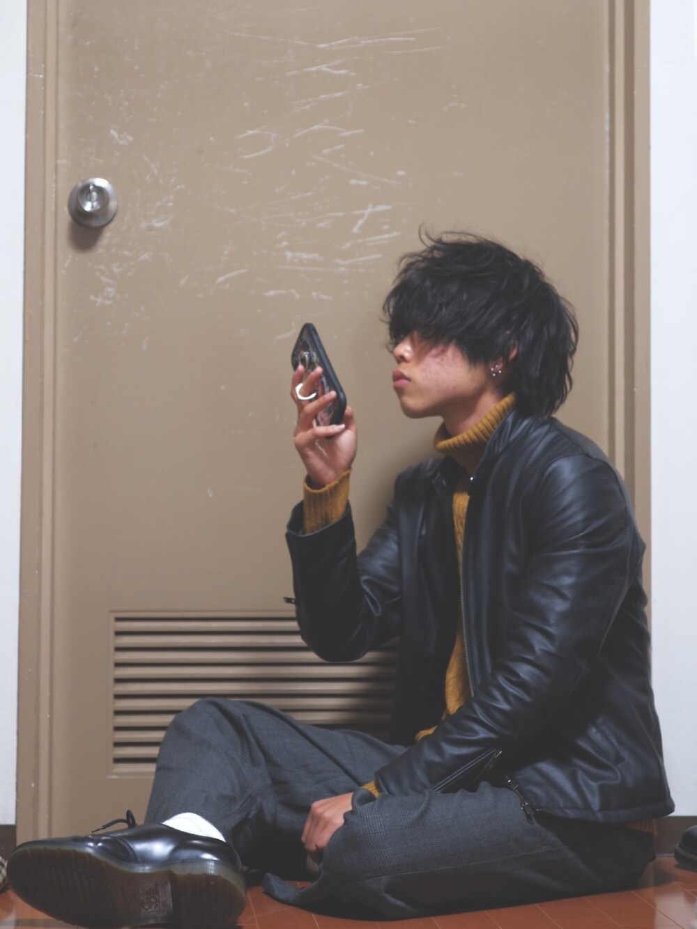 ブラック系のライダースジャケット、グレー系のスラックス、ブラック系のブーツを着用したメンズの秋コーディネートの1枚目の写真