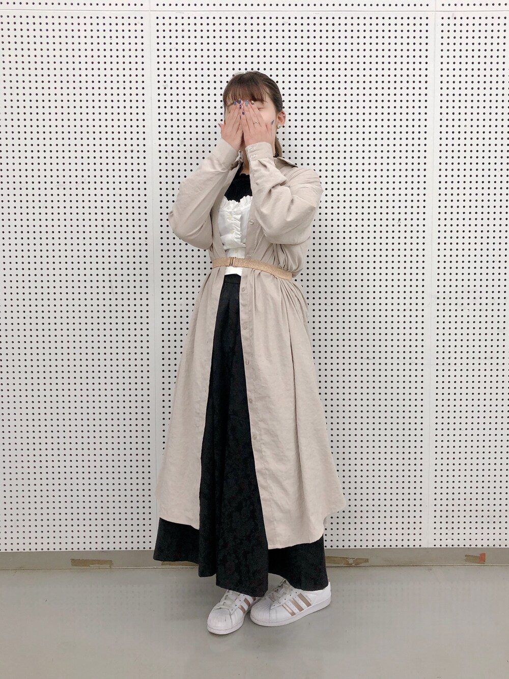 ベージュ系のシャツワンピース、ブラック系のスカート、ホワイト系のスニーカーを着用したレディースの秋コーディネートの1枚目の写真