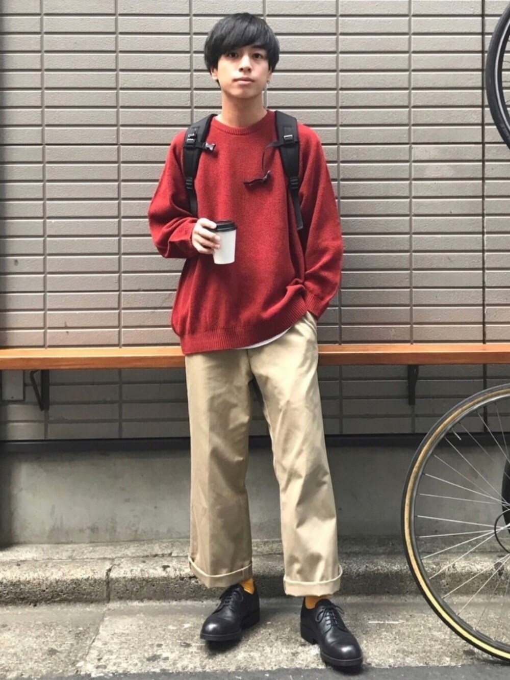 オレンジ系のニット/セーター、ベージュ系のチノパンツ、ブラック系のバックパック/リュックを着用したメンズの秋コーディネートの1枚目の写真