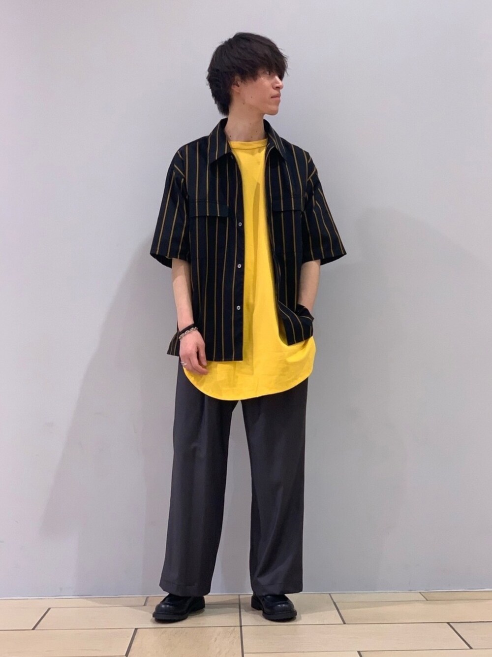 ブラック系のトップス、イエロー系のTシャツ/カットソー、グレー系のスラックスを着用したメンズの春コーディネートの1枚目の写真