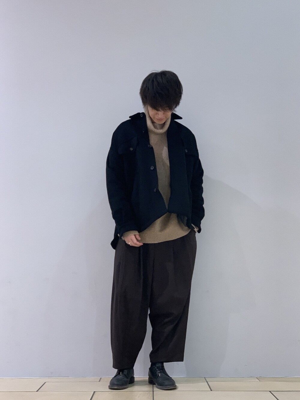 ブラック系のジャケット/アウター、ベージュ系のニット/セーター、ブラウン系のスラックスを着用したメンズの冬コーディネートの1枚目の写真