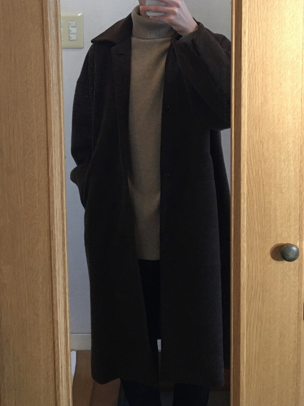 ブラウン系のステンカラーコート、ベージュ系のニット/セーター、ブラック系のスラックスを着用したメンズの冬コーディネートの1枚目の写真