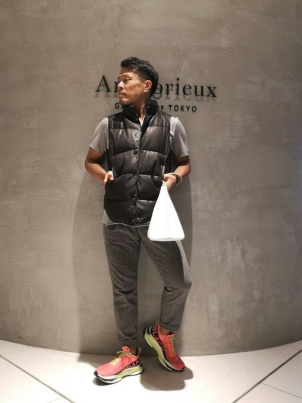 ホワイト系のハンドバッグ、ピンク系のスニーカー、ブラック系のダウンベストを着用したメンズの秋コーディネートの1枚目の写真