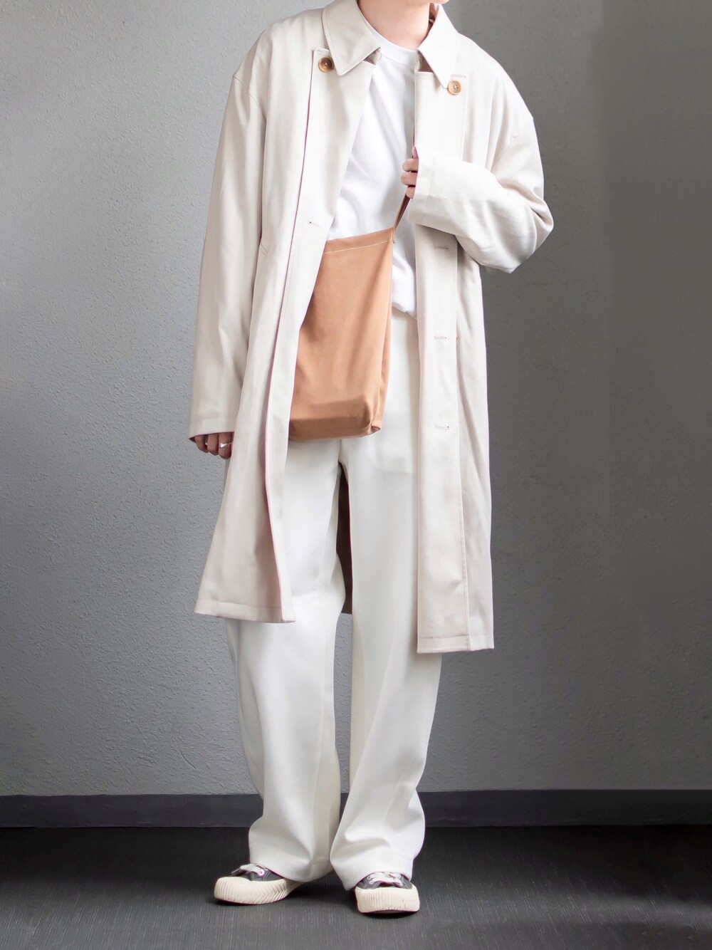 ベージュ系のトレンチコート、ホワイト系のTシャツ/カットソー、ベージュ系のショルダーバッグを着用したメンズの秋コーディネートの1枚目の写真