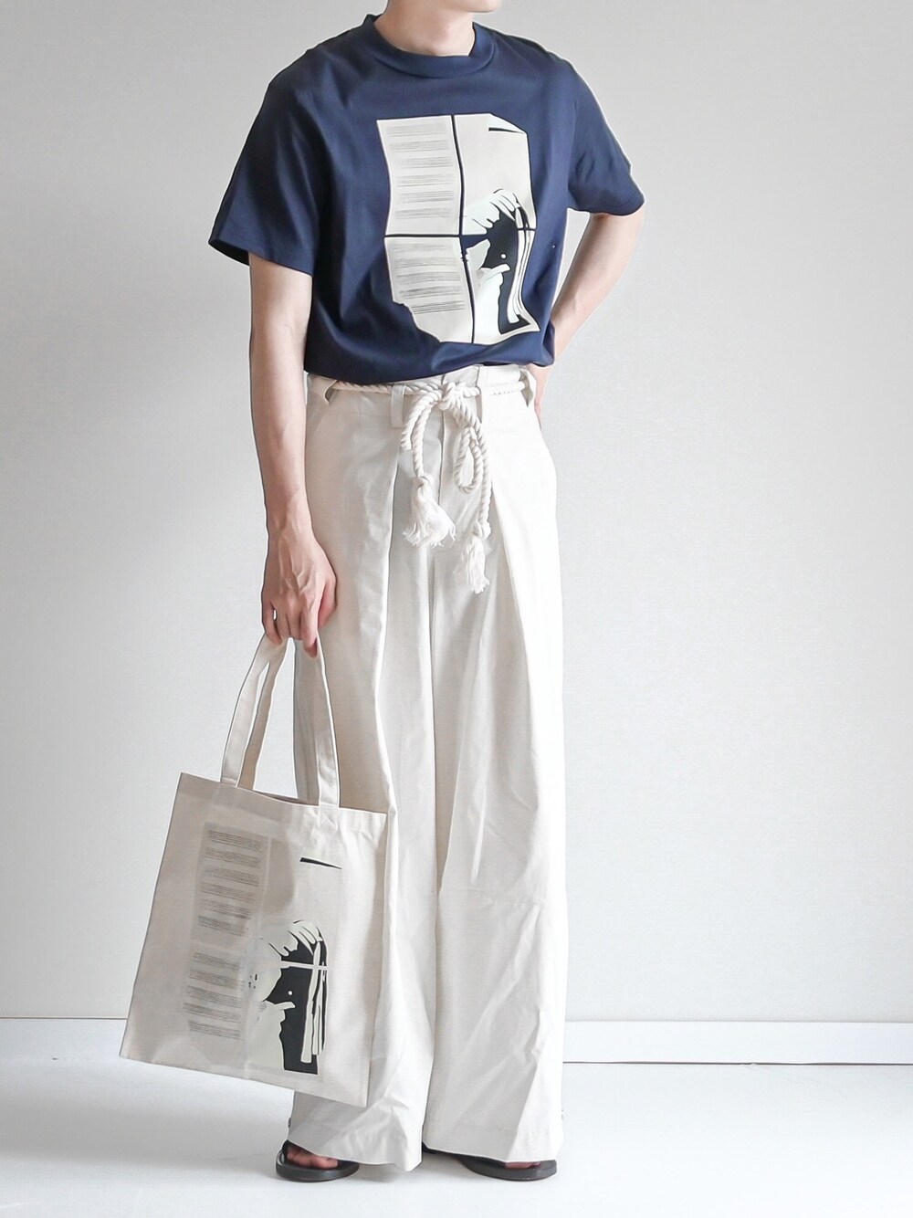 ブルー系のTシャツ/カットソー、ホワイト系のパンツ、ベージュ系のトートバッグを着用したメンズの夏コーディネートの1枚目の写真