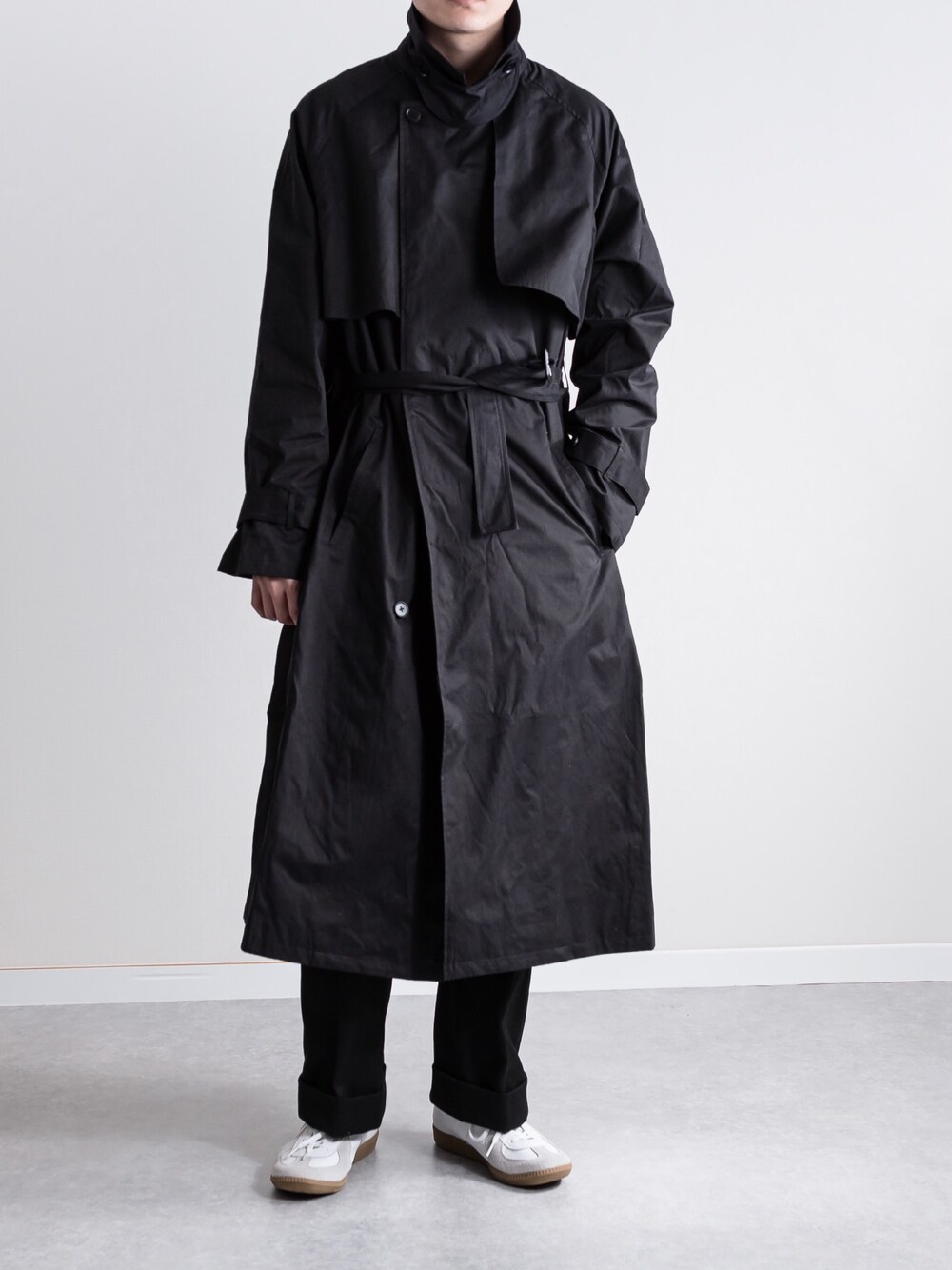 ブラック系のトレンチコート、ブラック系のパンツ、ホワイト系のスニーカーを着用したメンズの冬コーディネートの1枚目の写真