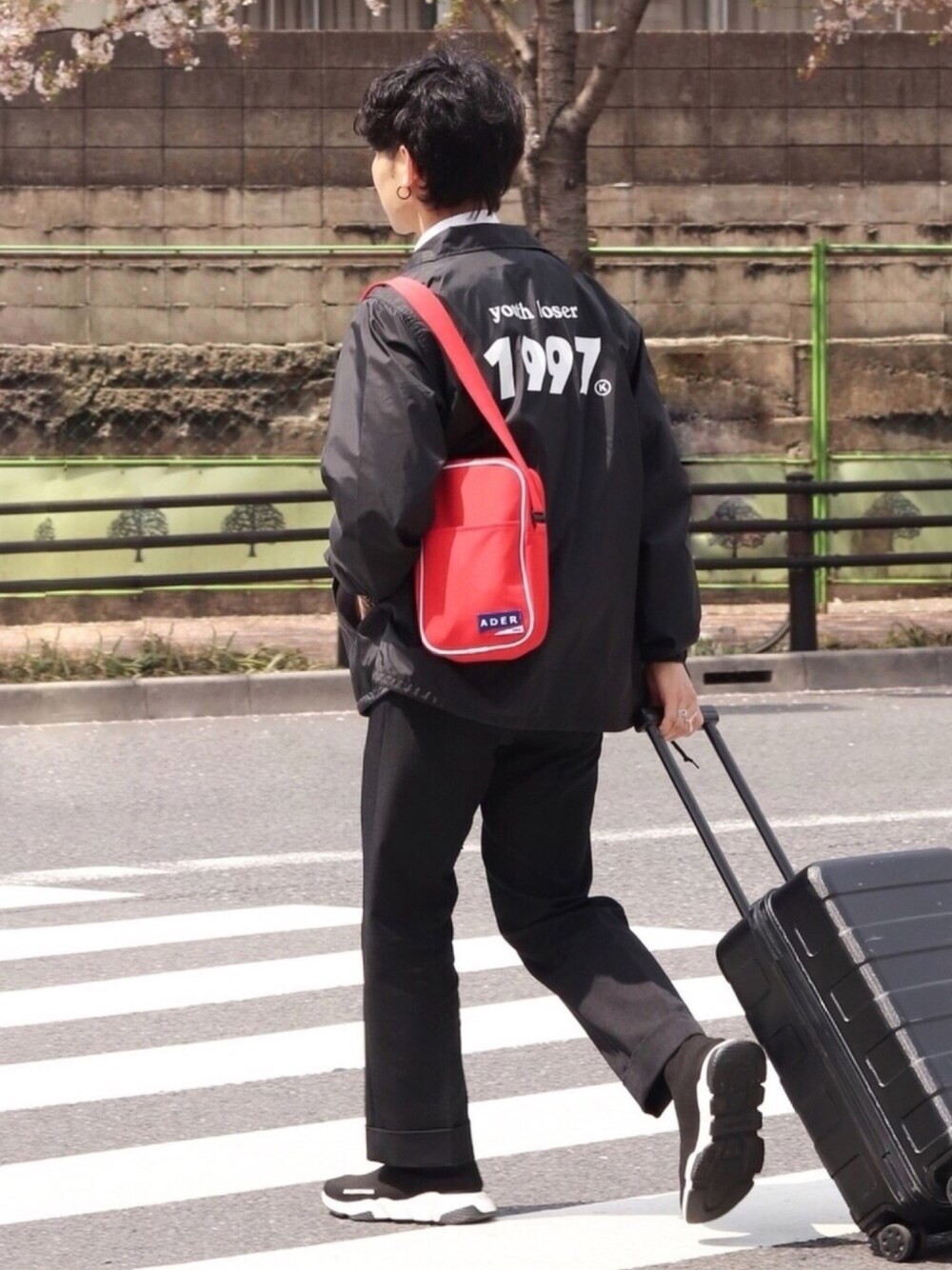 レッド系のショルダーバッグ、ブラック系のチノパンツ、ブラック系のスニーカーを着用したメンズの春コーディネートの1枚目の写真