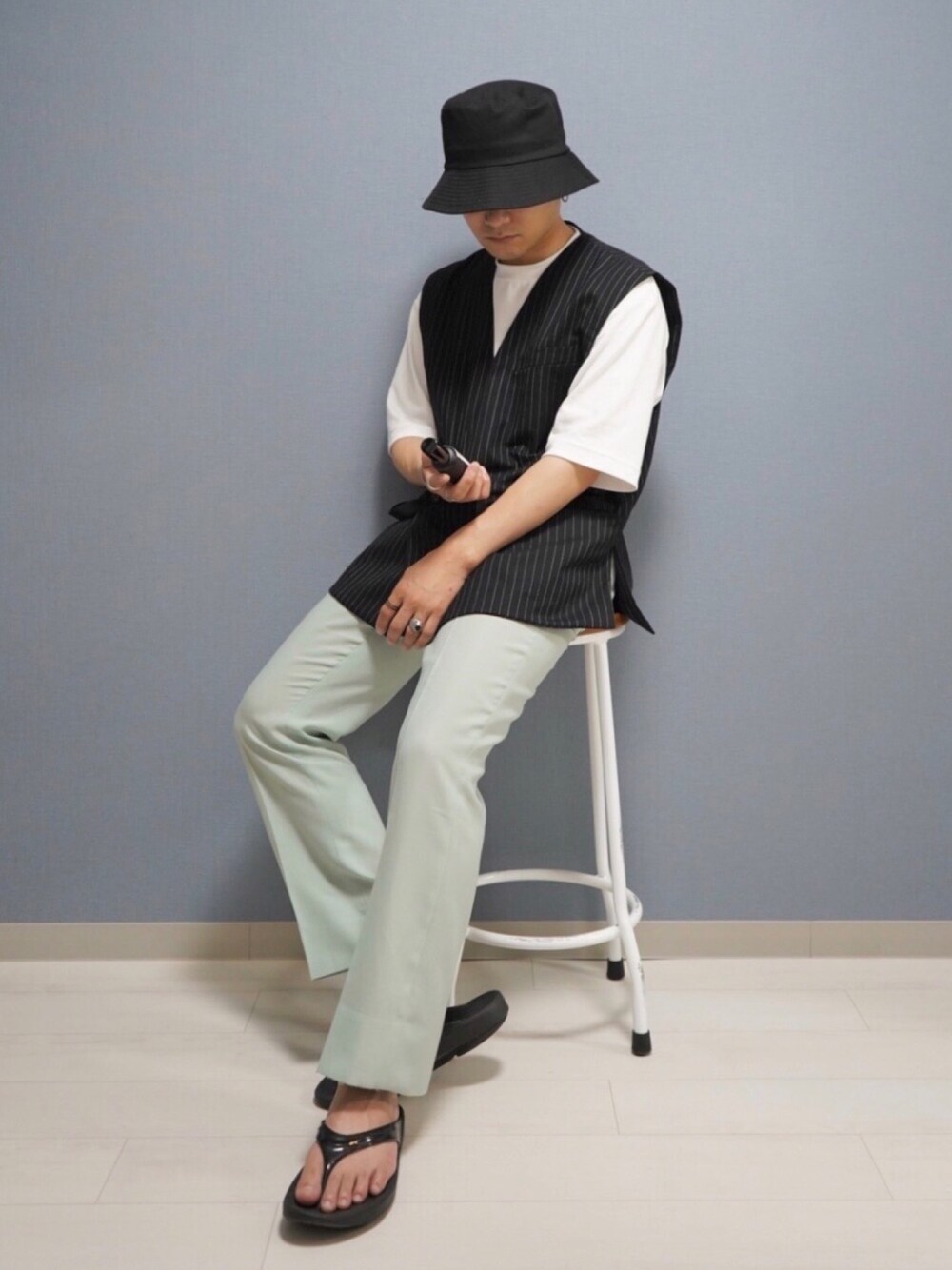 グリーン系のスラックス、ブラック系のサンダル、ブラック系のベストを着用したメンズの夏コーディネートの1枚目の写真