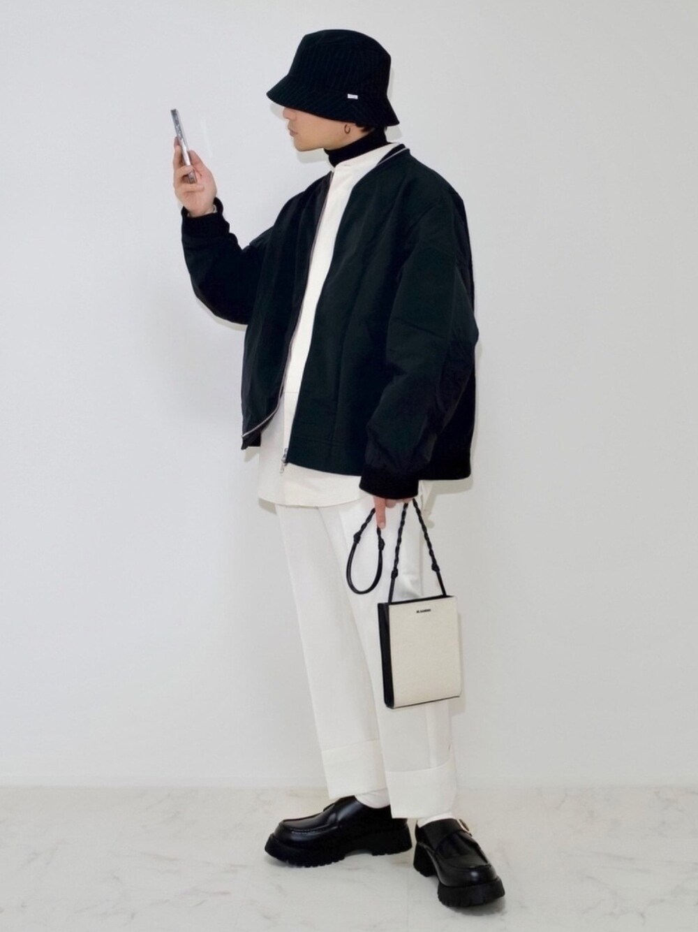 ホワイト系のスラックス、ホワイト系のショルダーバッグ、ブラック系のローファーを着用したメンズの冬コーディネートの1枚目の写真