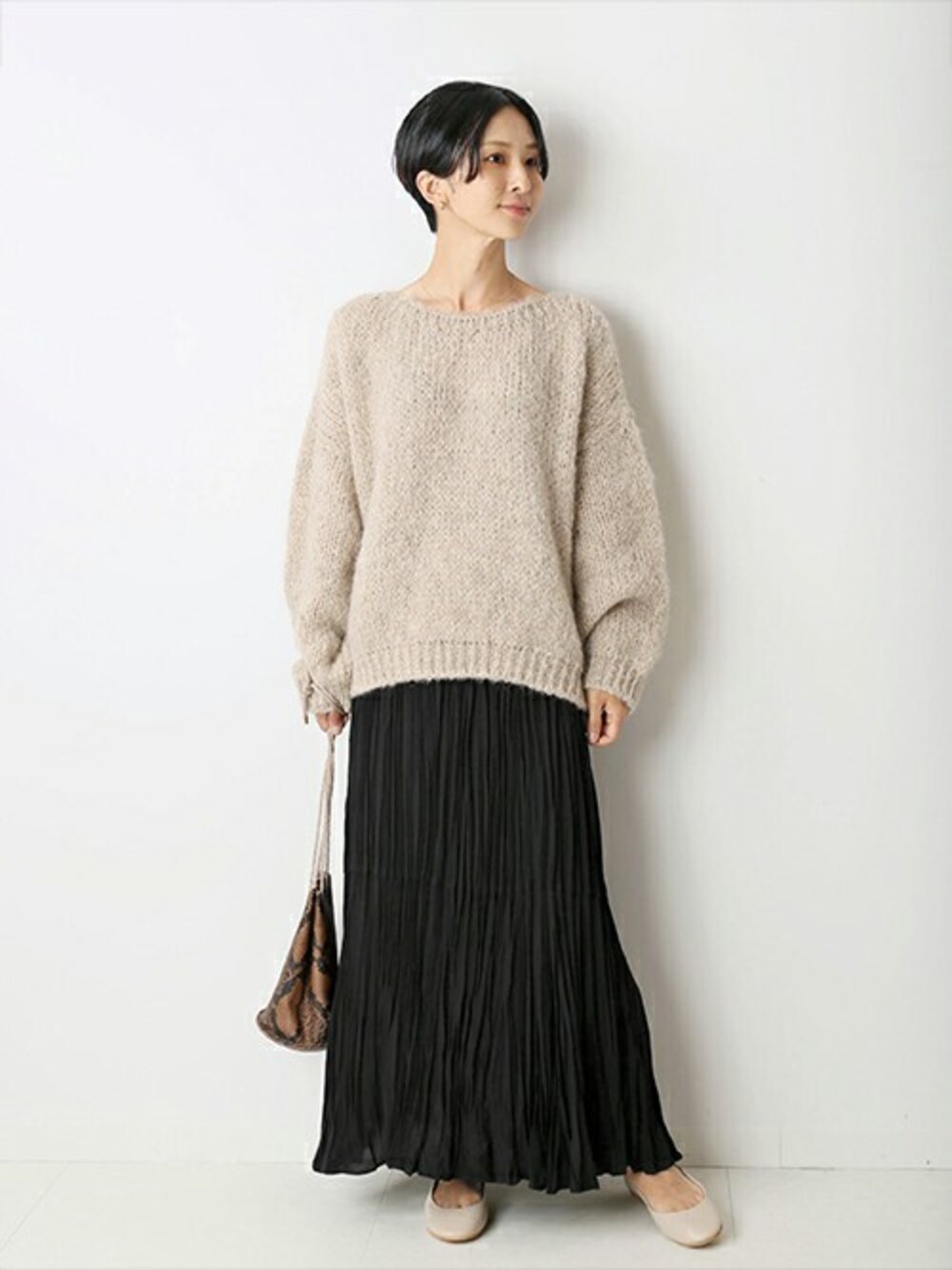 ブラック系のスカート、ベージュ系のニット/セーター、ブラウン系のショルダーバッグを着用したレディースの秋コーディネートの1枚目の写真