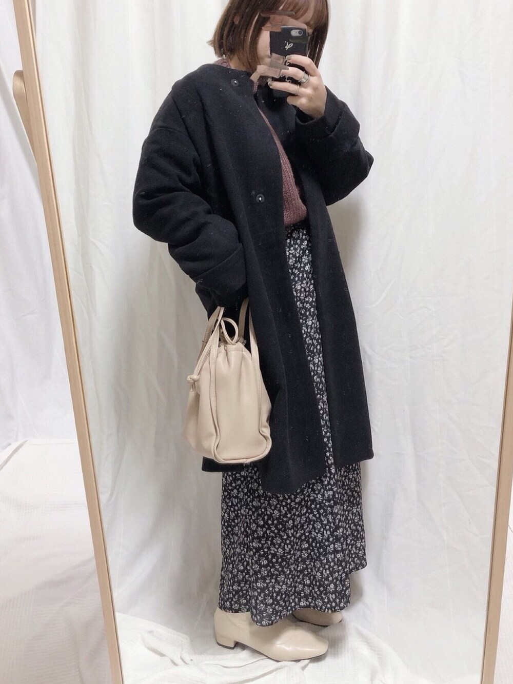 ブラック系のノーカラーコート、ベージュ系のショルダーバッグ、ホワイト系のブーツを着用したレディースの冬コーディネートの1枚目の写真