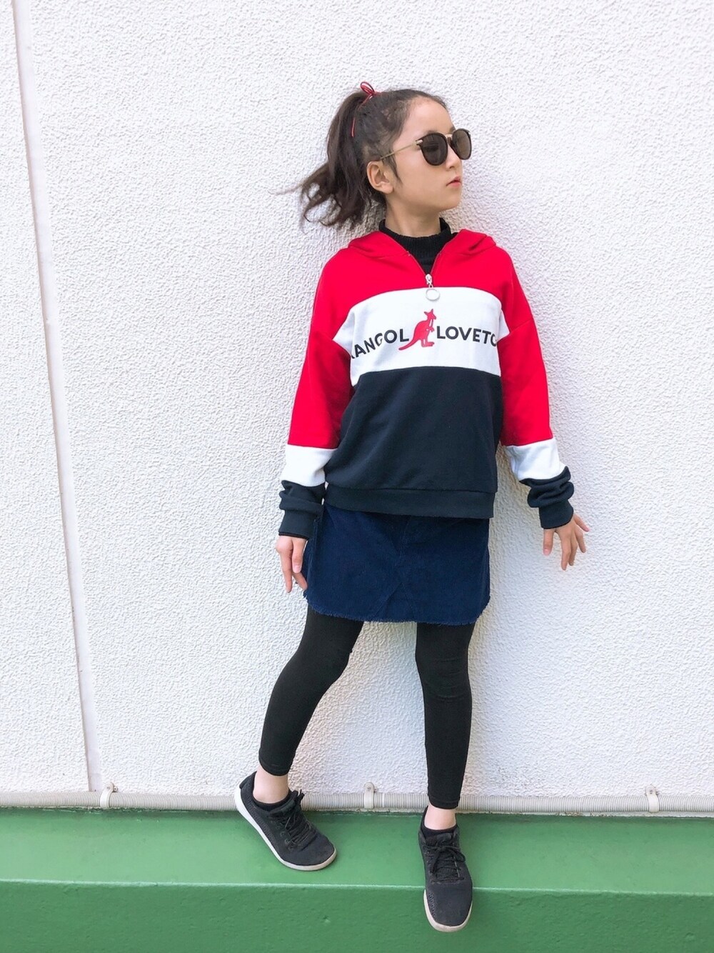 レッド系のパーカー、ブルー系のスカート、ブラック系のスニーカーを着用したキッズの秋コーディネートの1枚目の写真