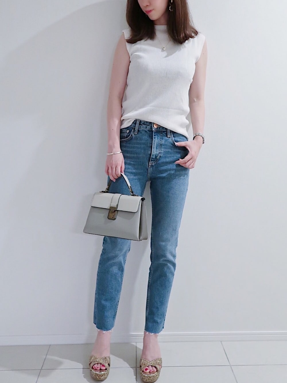ホワイト系のニット/セーター、ブルー系のデニムパンツ、グレー系のバッグを着用したレディースの夏コーディネートの1枚目の写真