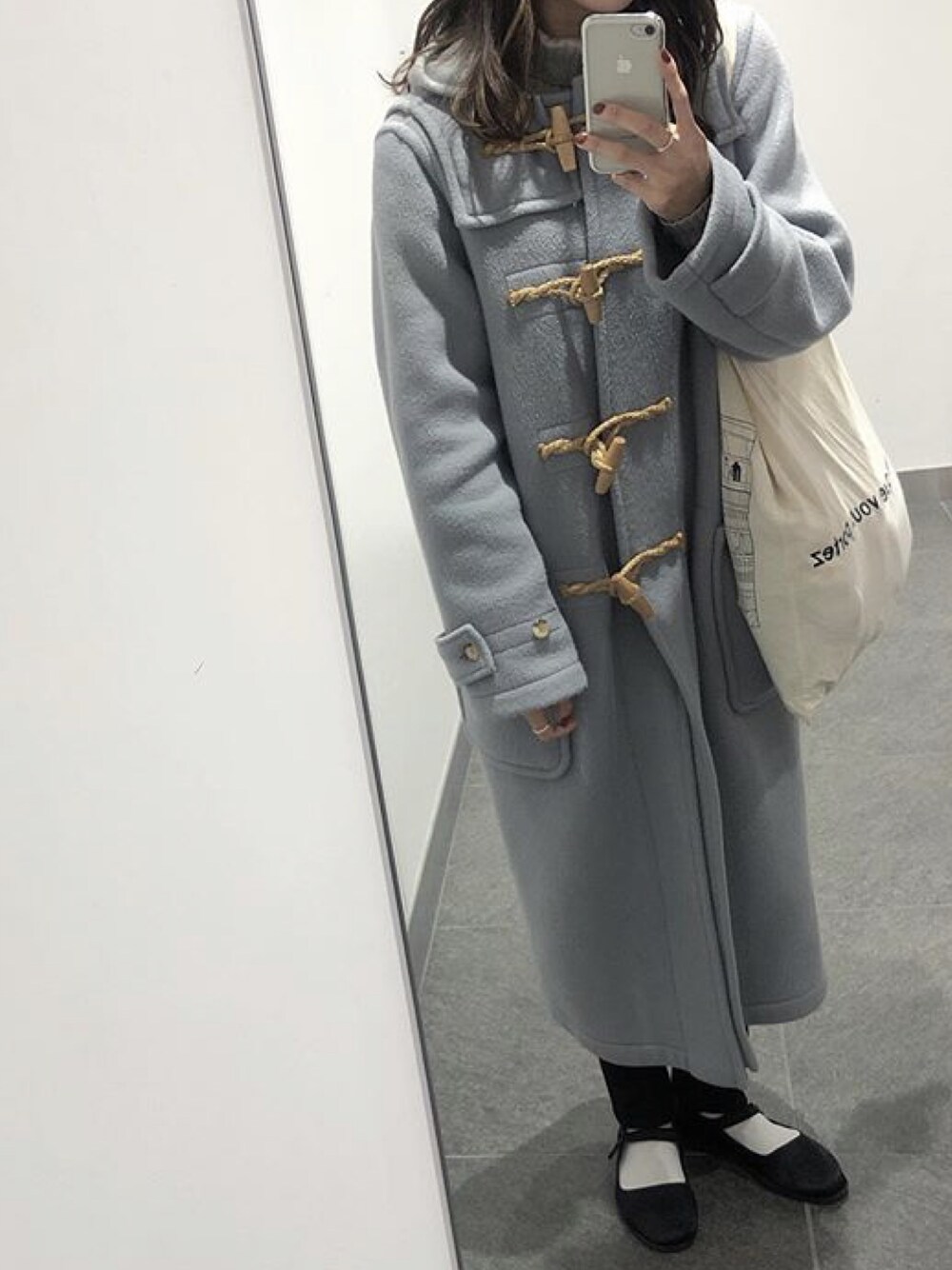 ブルー系のダッフルコート、ホワイト系のトートバッグ、ブラック系のその他シューズを着用したレディースの冬コーディネートの1枚目の写真