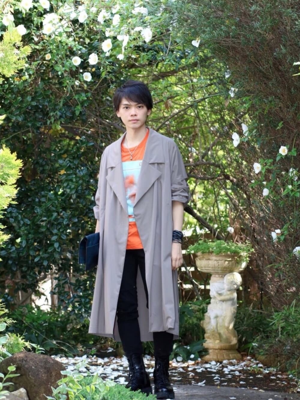 ベージュ系のその他アウター、ブラック系のクラッチバッグ、オレンジ系のTシャツ/カットソーを着用したメンズの春コーディネートの1枚目の写真